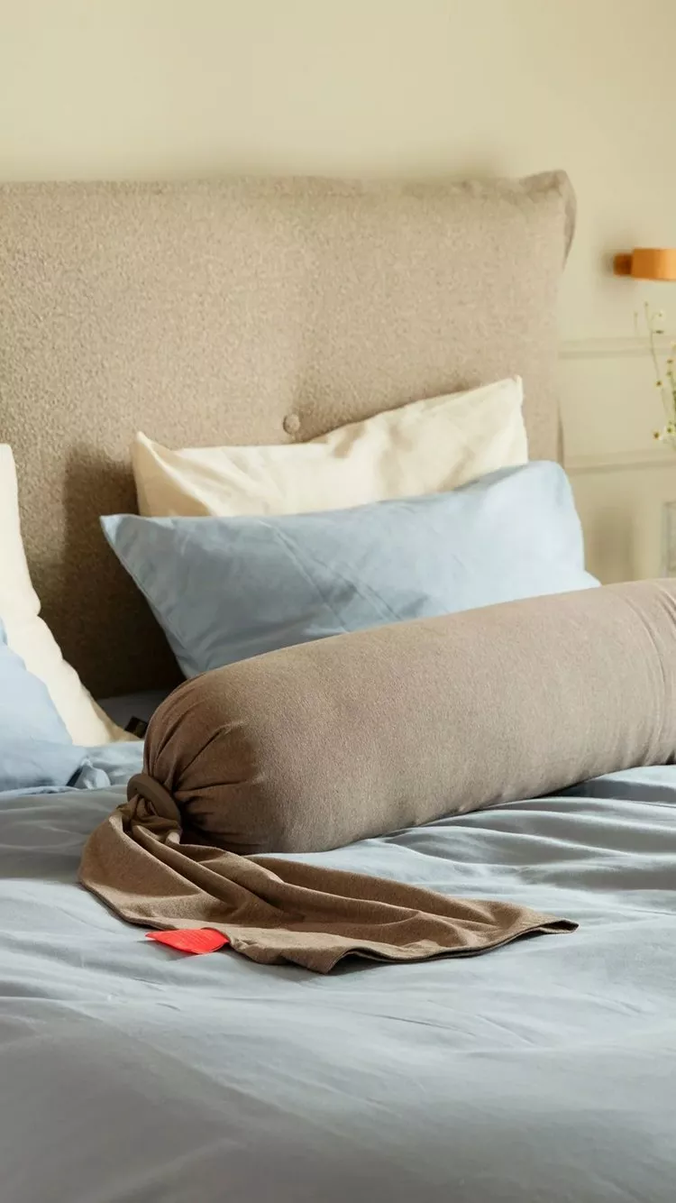 Modern bedroom with upholstered headboard, blue bedding and pregnancy pillow in soft natural light