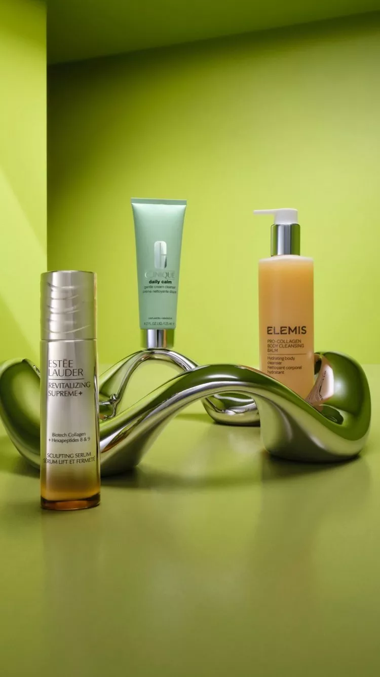 Estée Lauder serum, Clinique cream and Elemis body cleanser displayed on green background with metallic sculpture