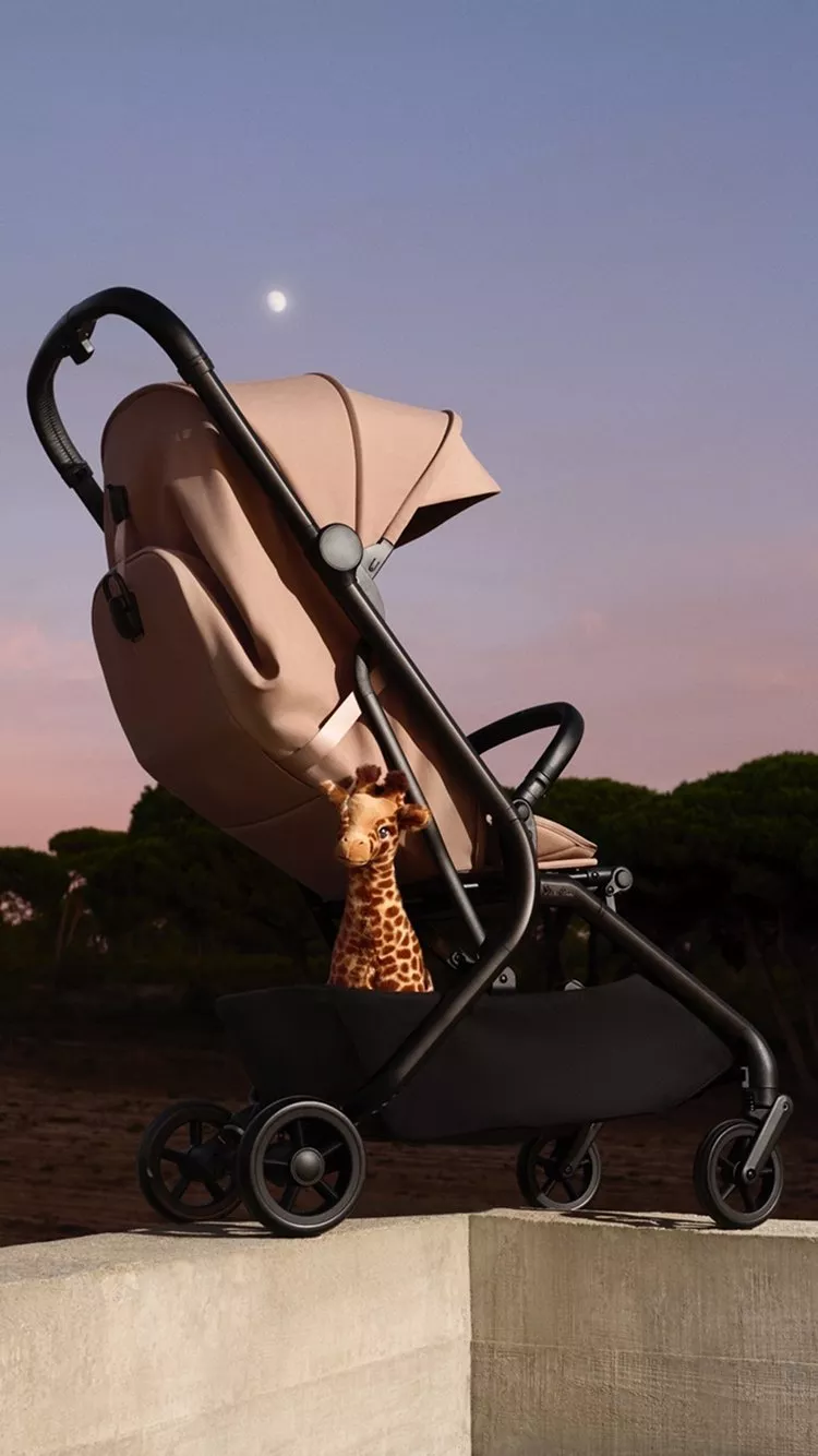 Beige baby pushchair and pram with a cute giraffe toy, outdoors at dusk under a pastel sky and moon