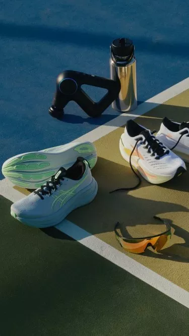 Running shoes, water bottle, massage gun and sports sunglasses on an outdoor court, fitness gear flat lay