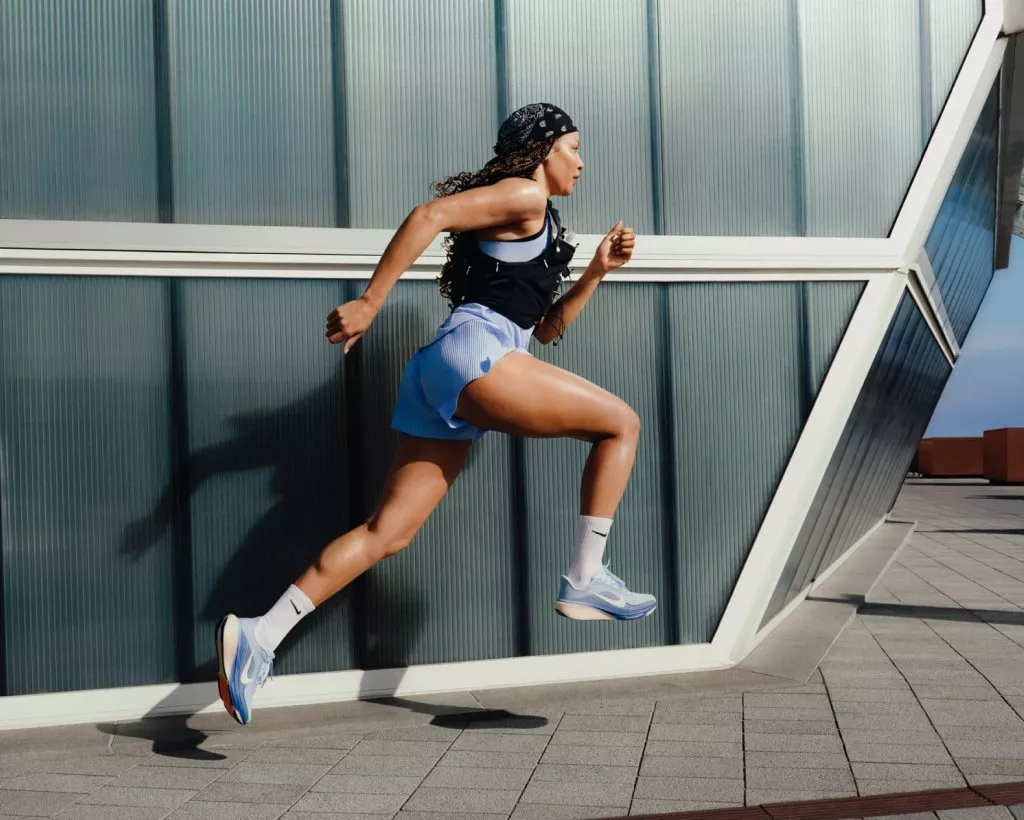 Female runner sprinting outdoors beside modern glass building, wearing sportswear and trainers in urban setting