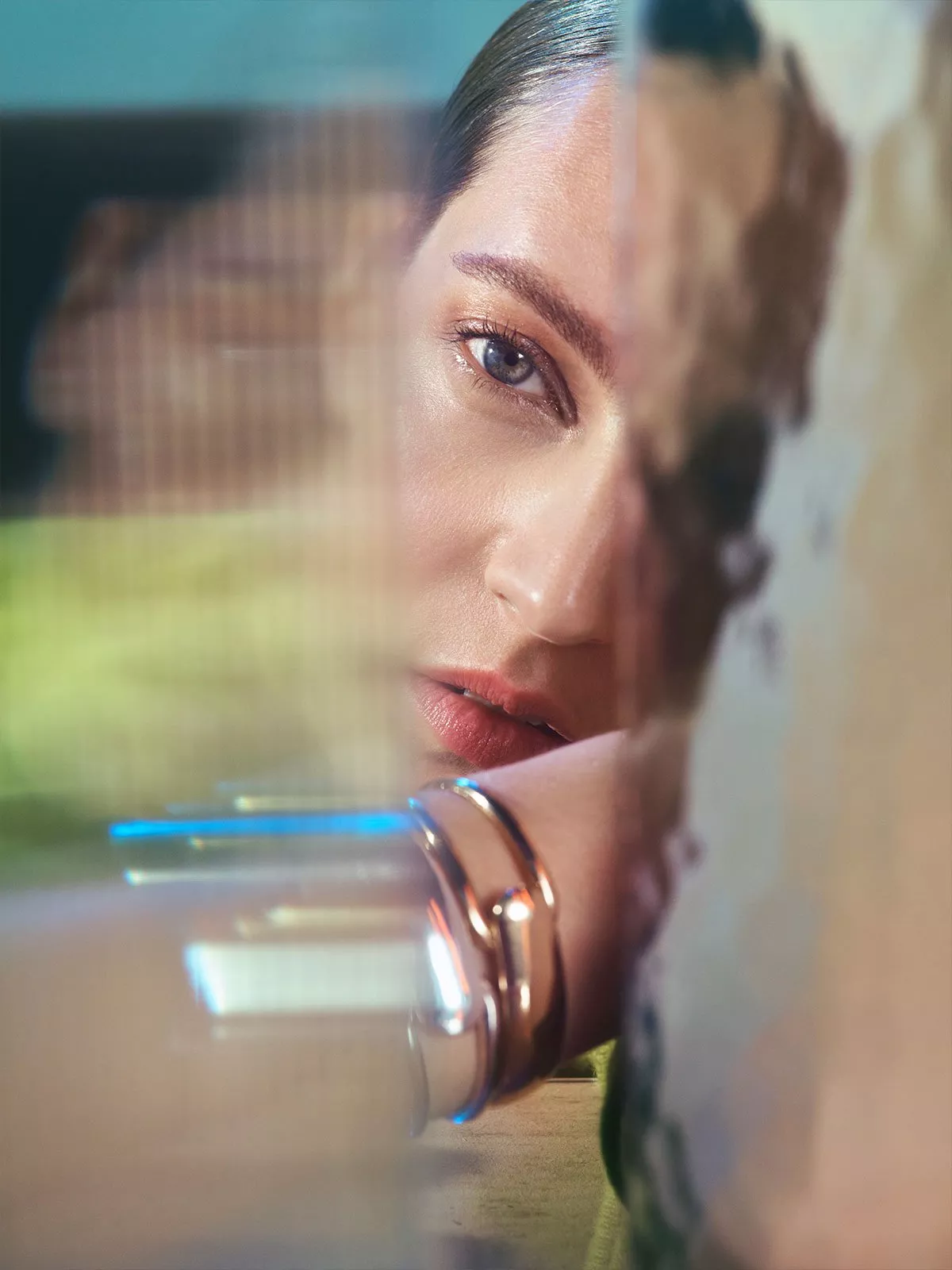 Artistic close-up portrait of a woman behind glass, soft reflections and silver bracelet, fashion photography style