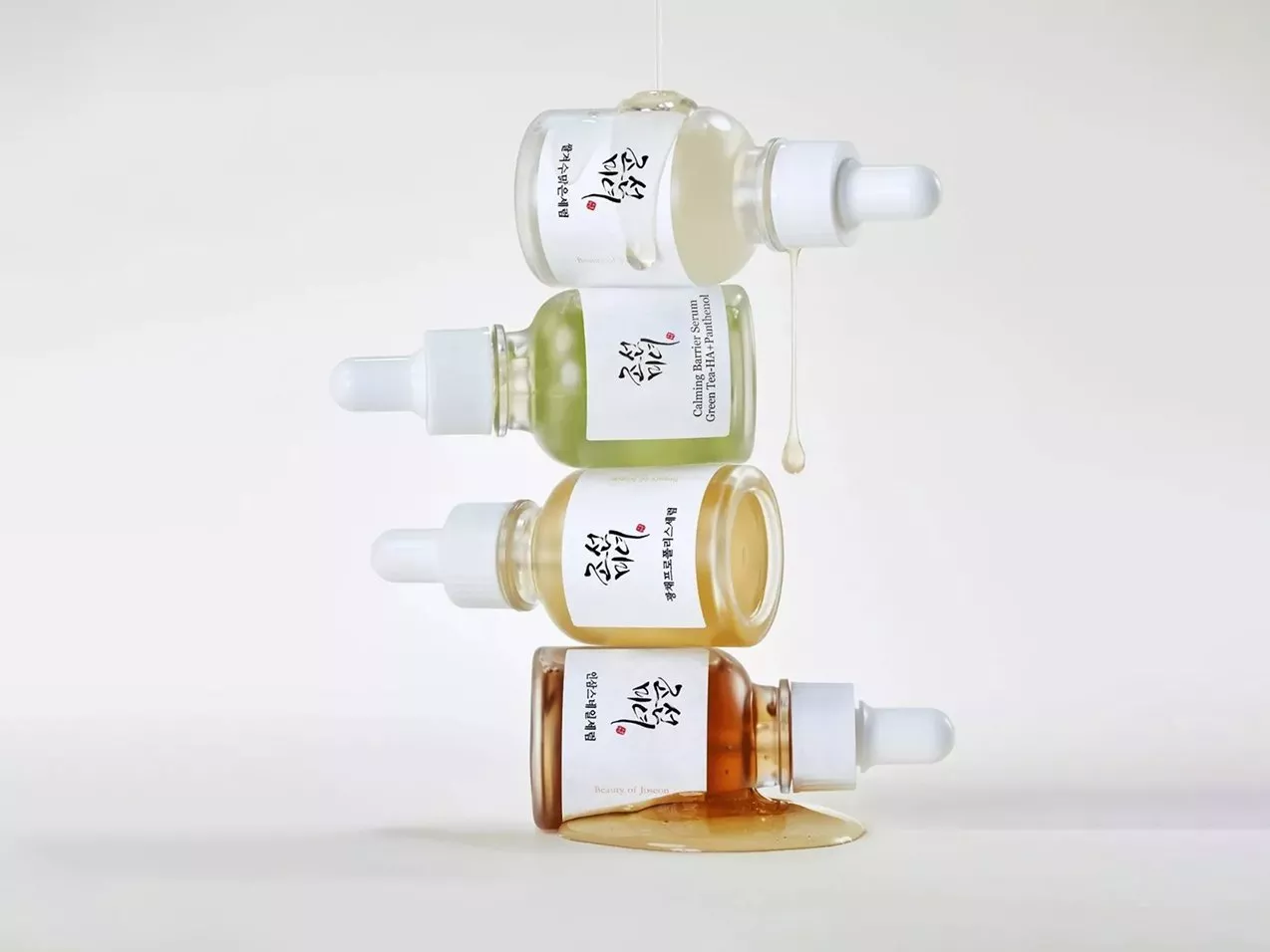 Stacked skincare serum dropper bottles with dripping liquid, minimalist product shot on a white background