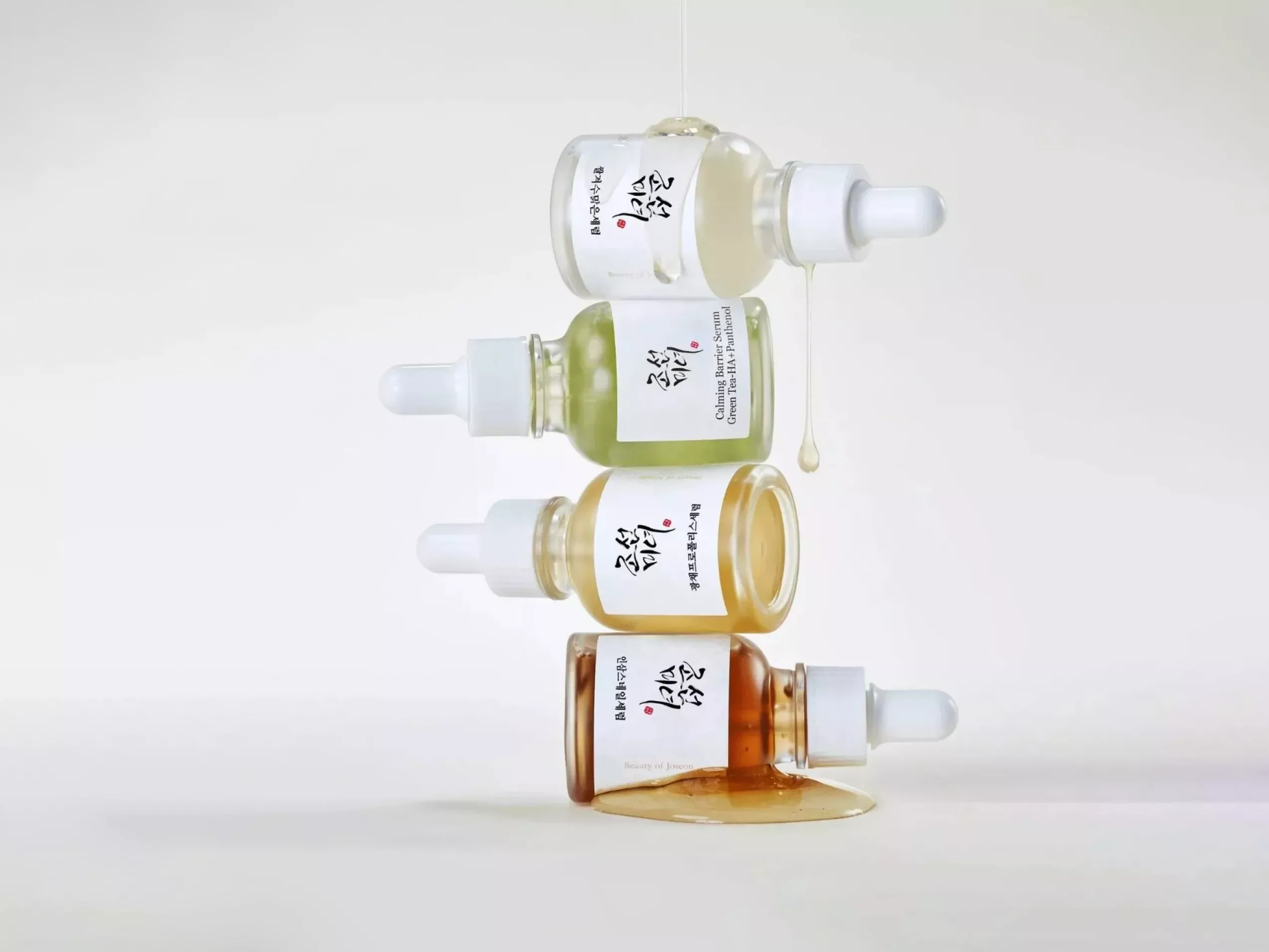 Stacked skincare serum dropper bottles with dripping essence, minimalist product photo on white background