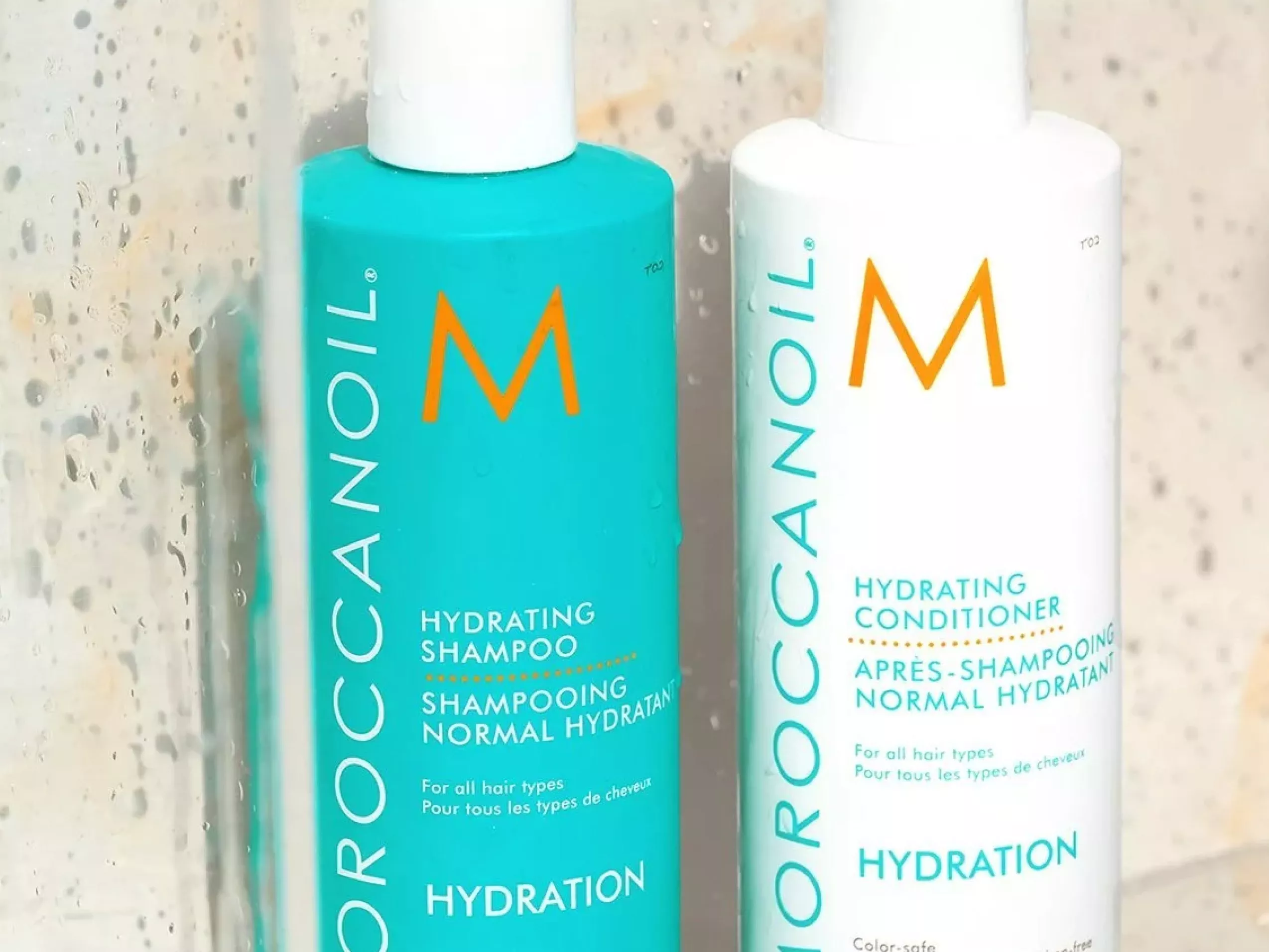 Moroccanoil Hydration shampoo and conditioner bottles in shower, turquoise and white haircare packaging close-up