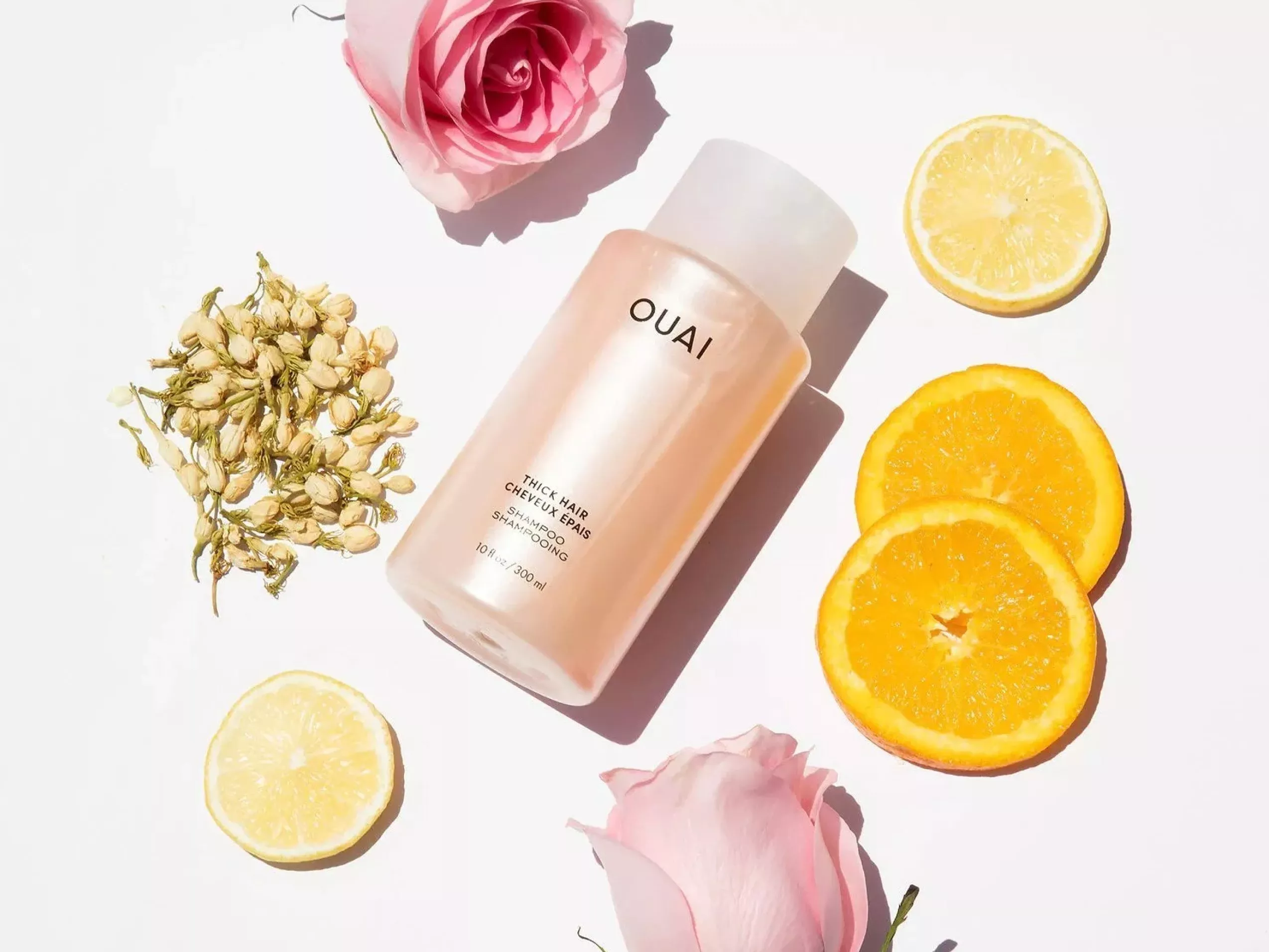 OUAI thick hair shampoo bottle flat lay with orange and lemon slices, rose petals and dried flowers on white background