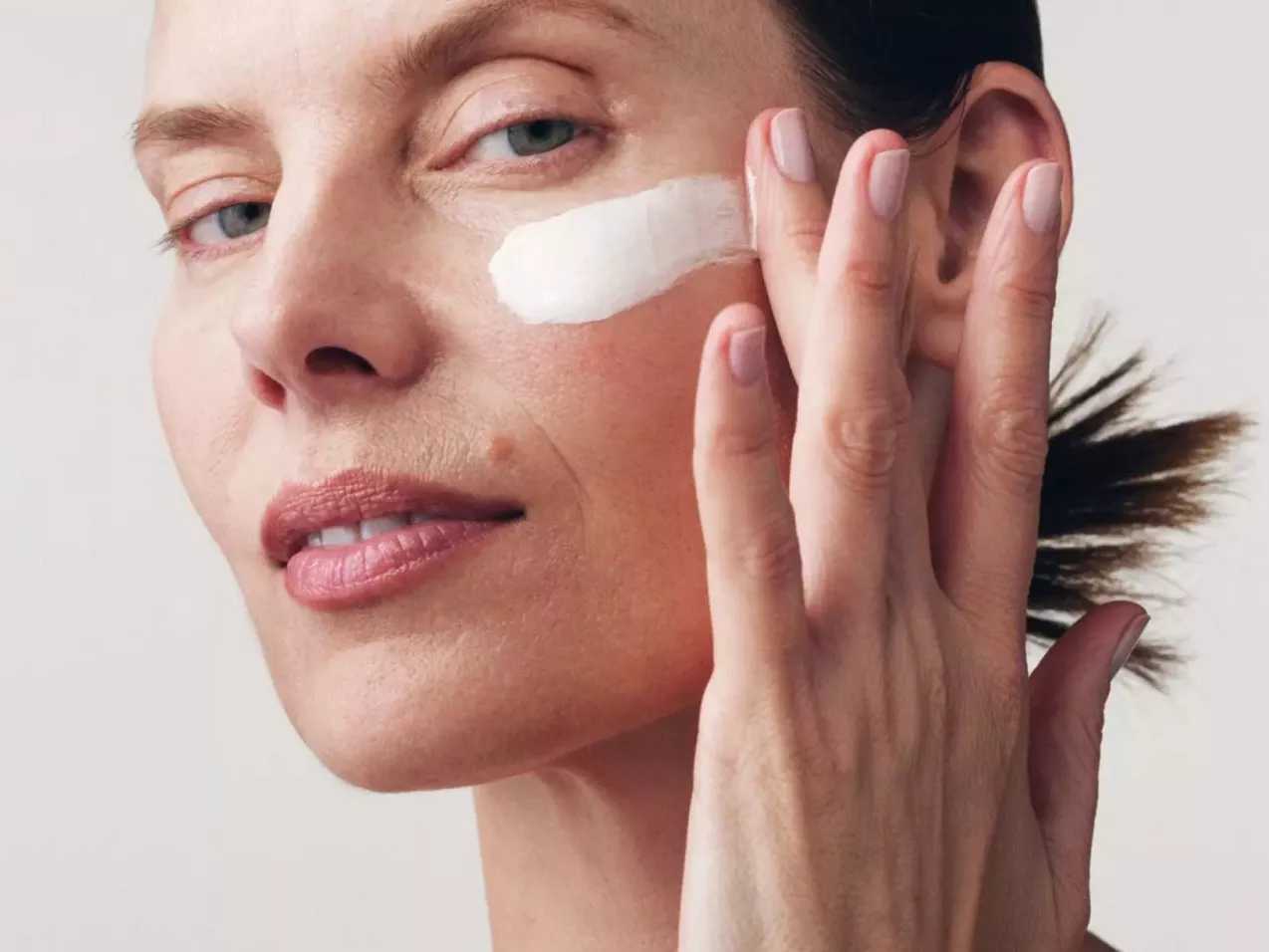 Image of a model putting cream on her face looking at the camera