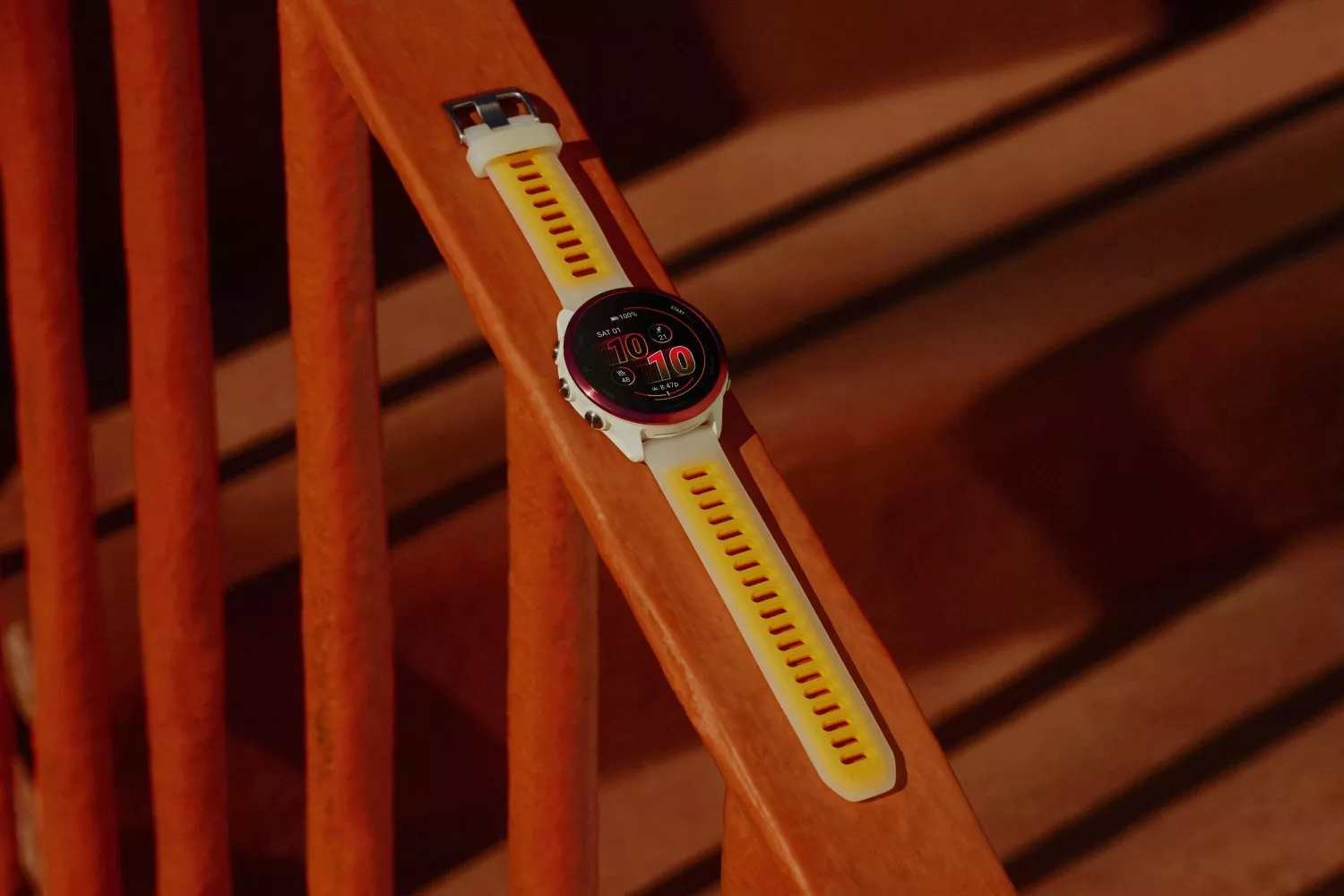 White and yellow GPS sports smartwatch with round digital face resting on wooden bench in warm light