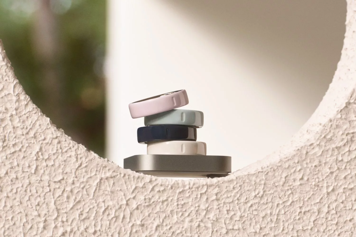 Stacked smart rings in pastel colours on a stand, minimalist product photo with soft outdoor background blur