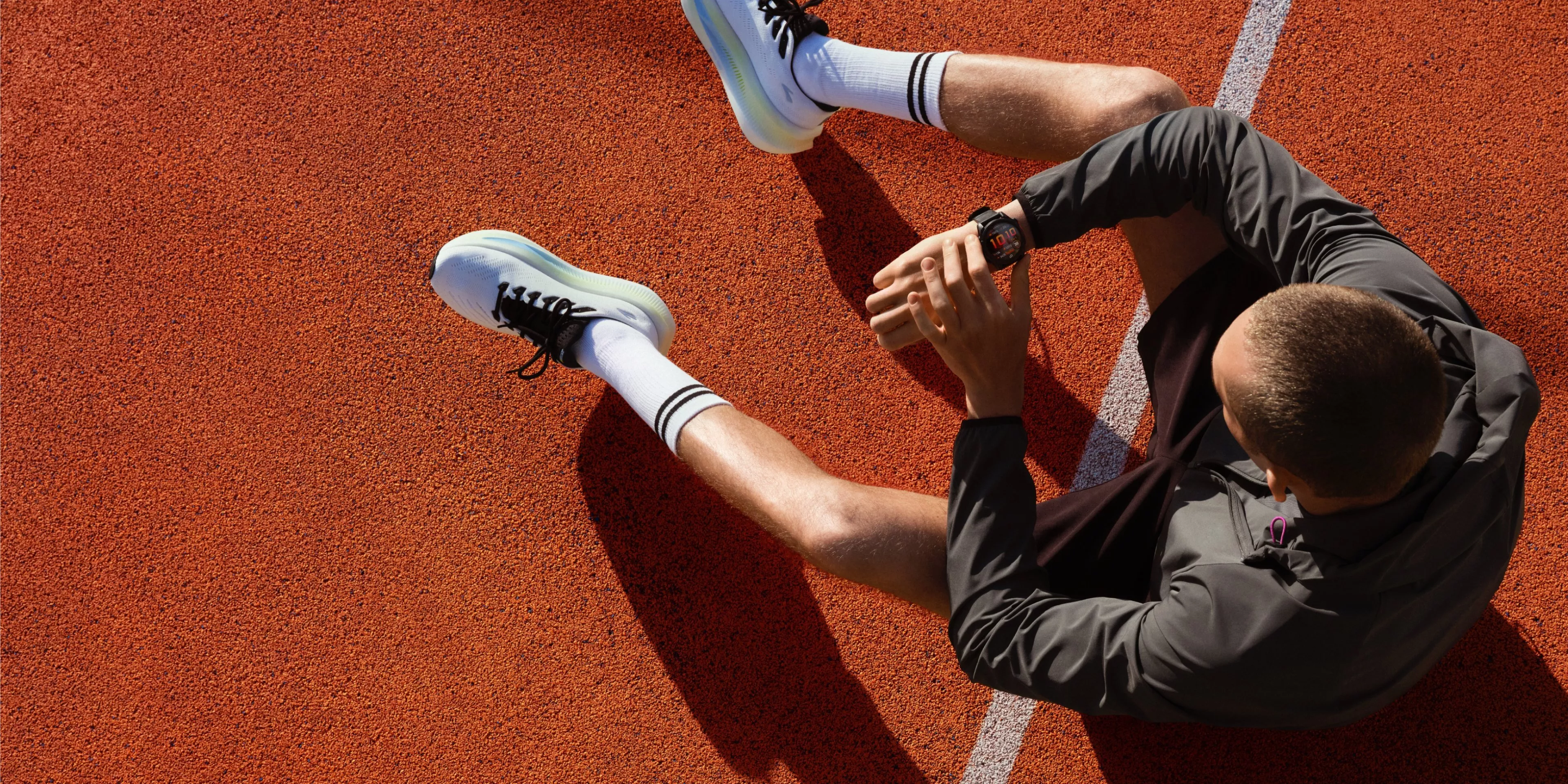 Overhead view of runner sitting on athletics track checking smartwatch, wearing running shoes and sportswear