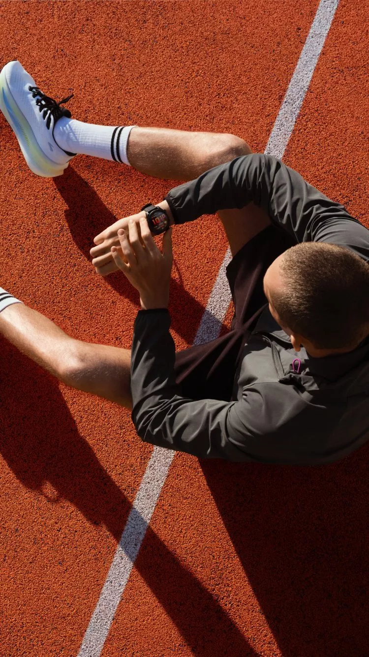 Overhead view of runner sitting on athletics track checking smartwatch, wearing running shoes and sportswear