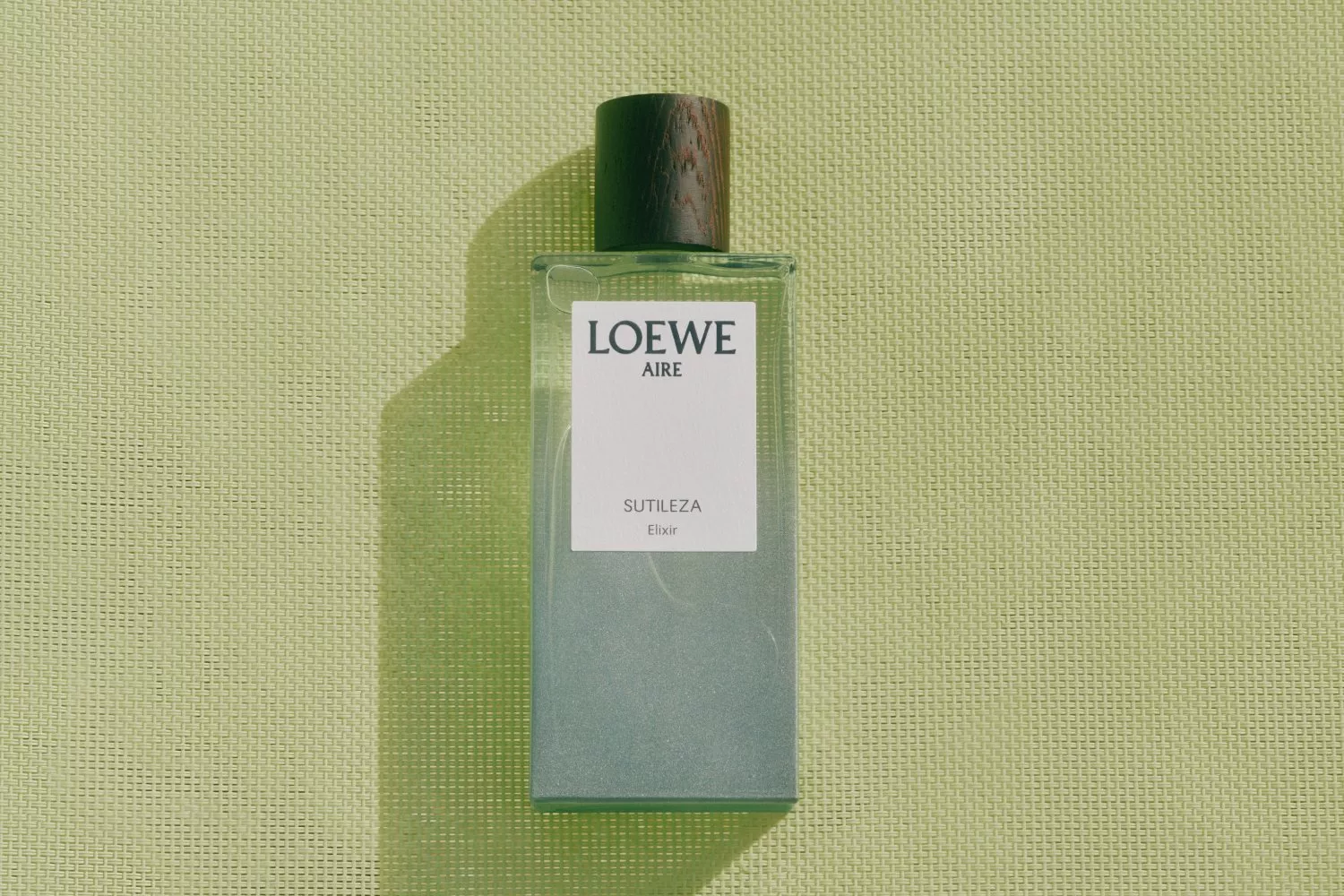 Loewe Aire Sutileza Elixir perfume bottle with wooden cap on textured green background, product flat lay photo