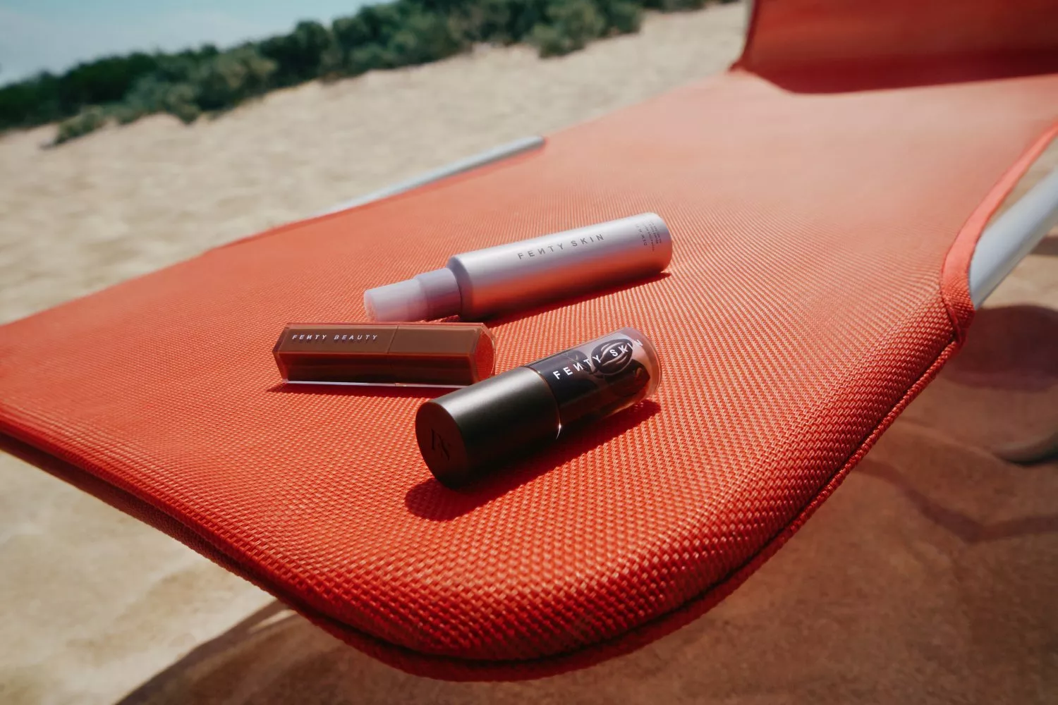 Fenty Beauty and Fenty Skin products on orange sun lounger at sandy beach, summer skincare and makeup flat lay