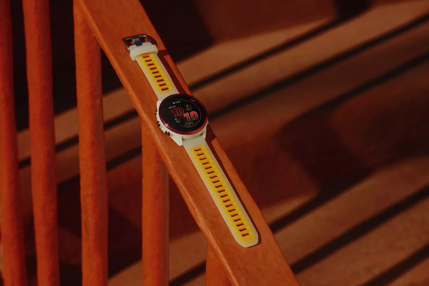 White and yellow GPS sports smartwatch with digital display resting on wooden chair slats in warm light