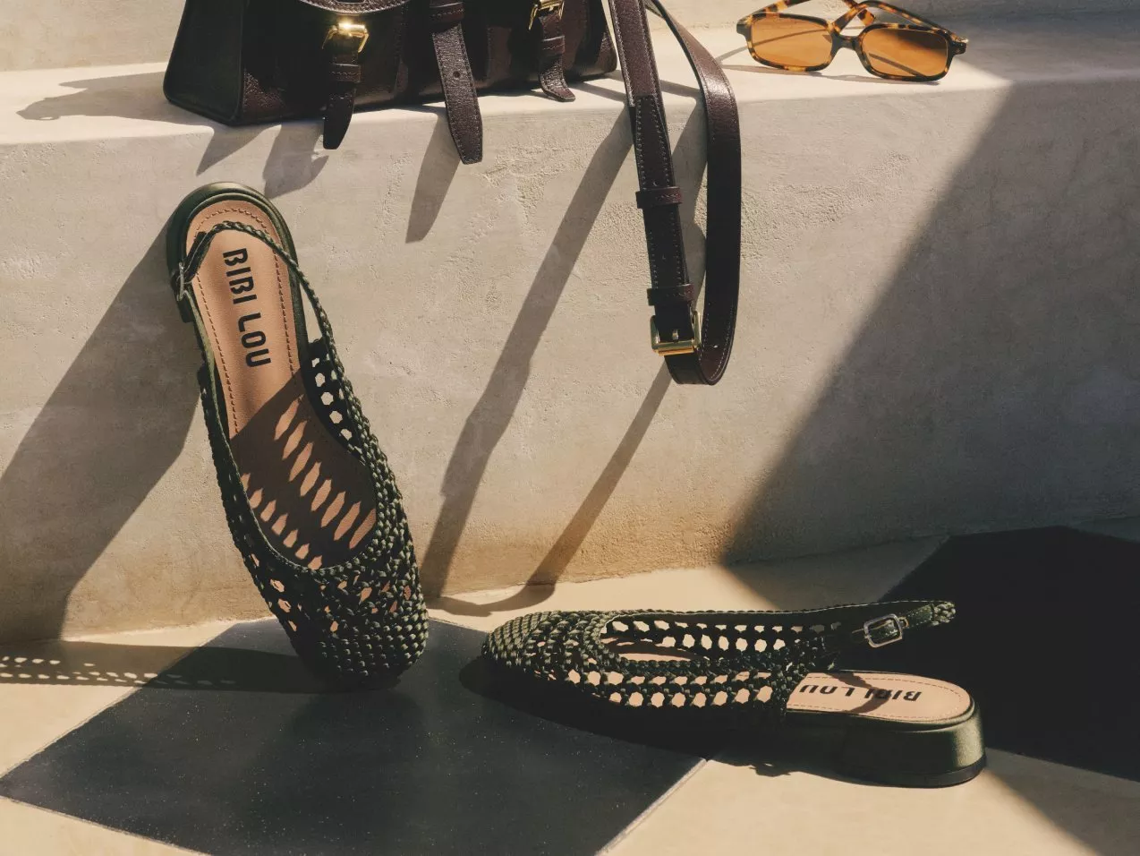 BIRI LOU woven green flats with leather handbag and sunglasses on sunlit concrete steps, fashion still life