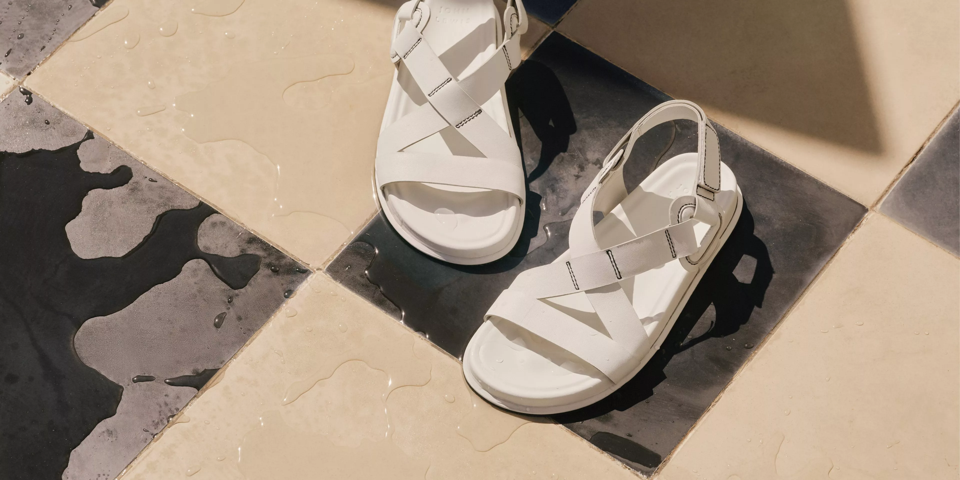 White leather strappy sandals on wet black and cream tiled floor, summer footwear product photo in sunlight