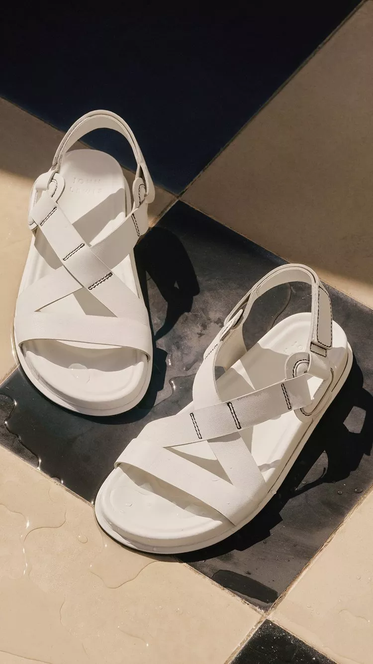 Pair of white leather strappy sandals on wet black and cream tiled floor in bright summer sunlight