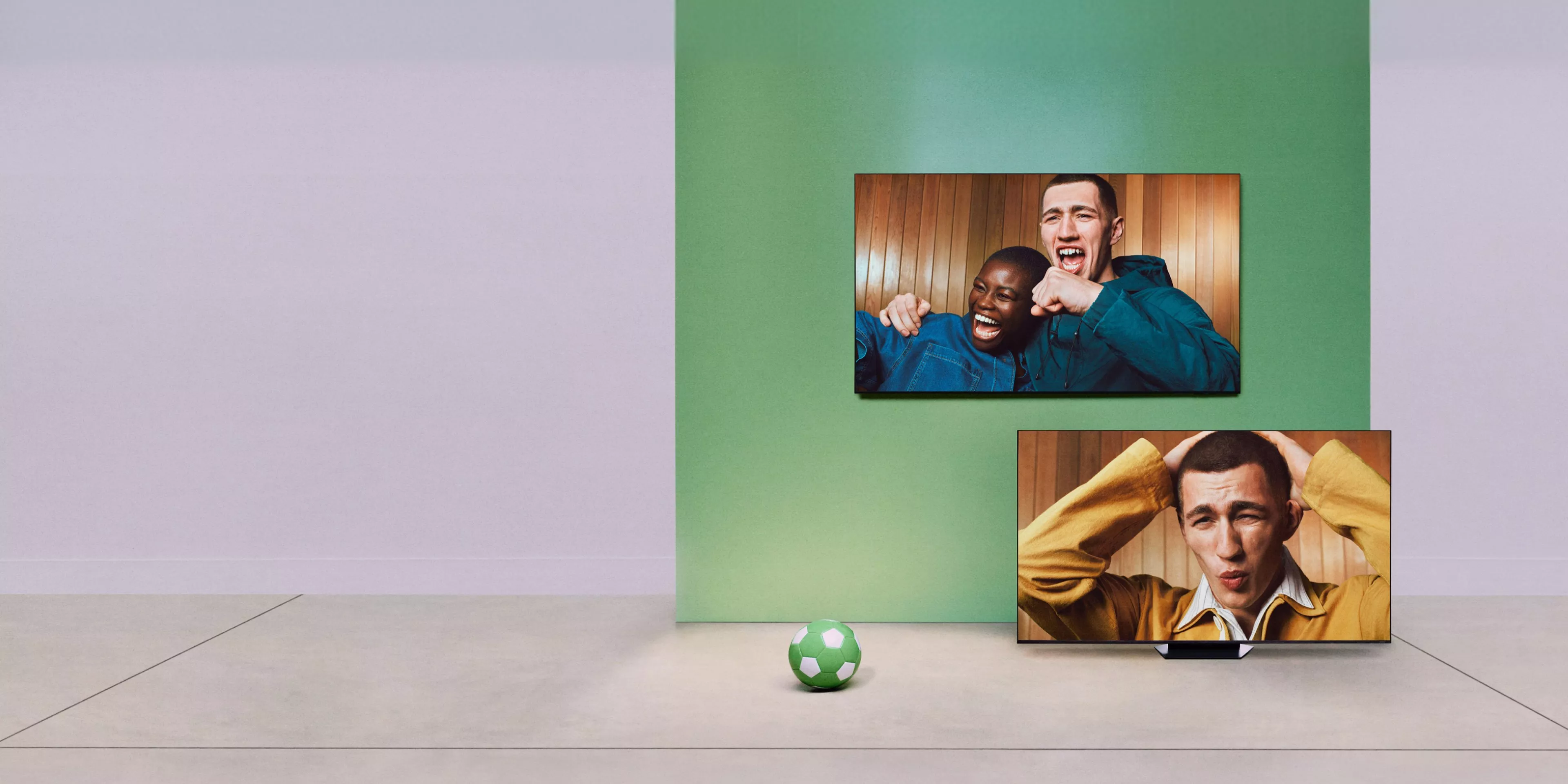Two TVs show football fans cheering and reacting, with a green football on the floor in a minimalist room.