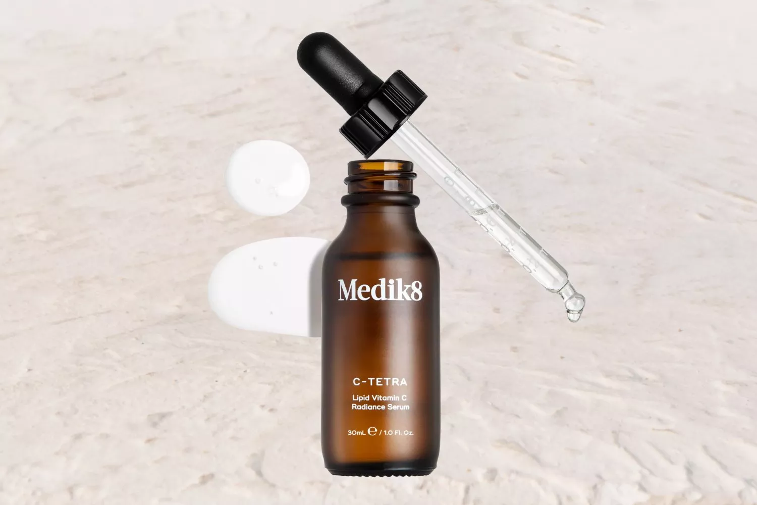 Medik8 C-Tetra serum bottle with a dropper on a textured surface, showcasing skincare product details.