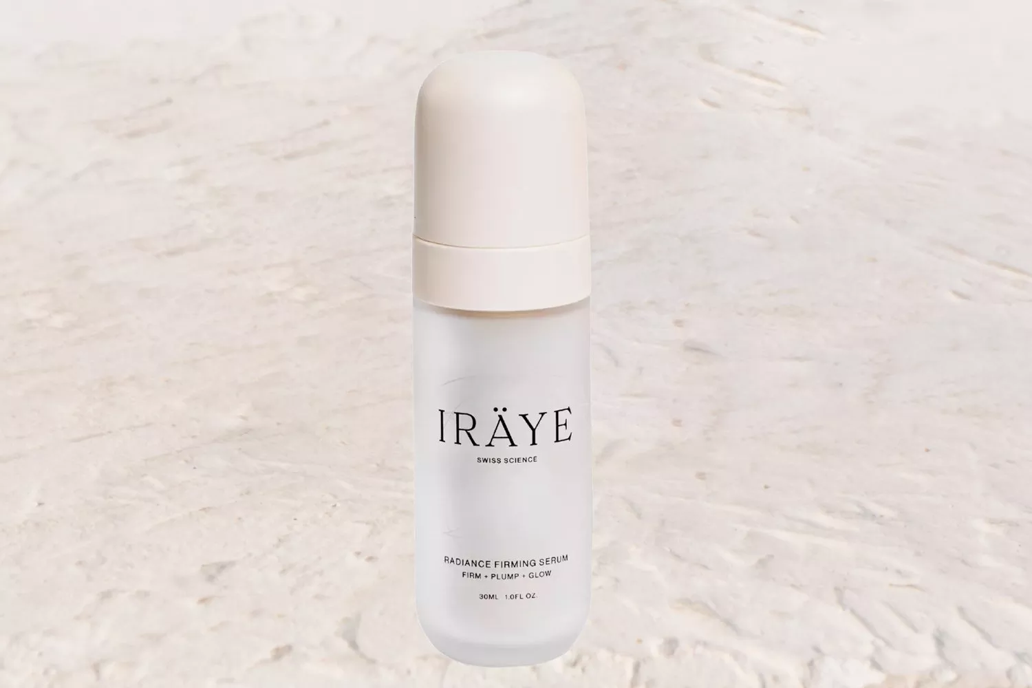 A clear bottle of IRÄYE Radiance Firming Serum with a white cap on a light textured background.