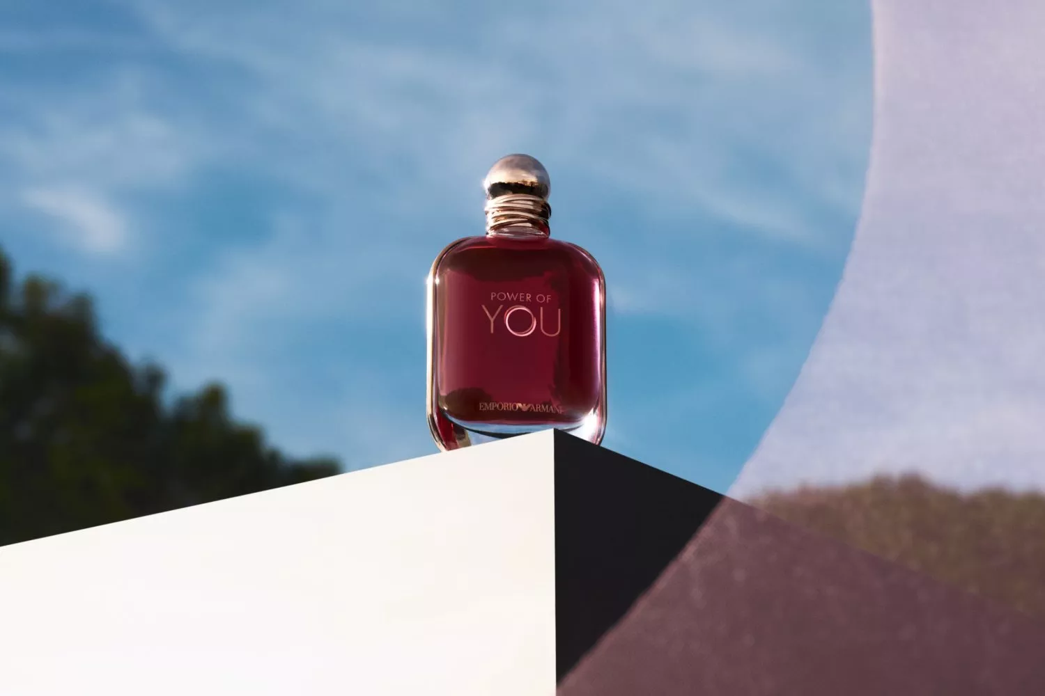 Emporio Armani Power of You red perfume bottle on white pedestal, outdoor product shot with blue sky backdrop