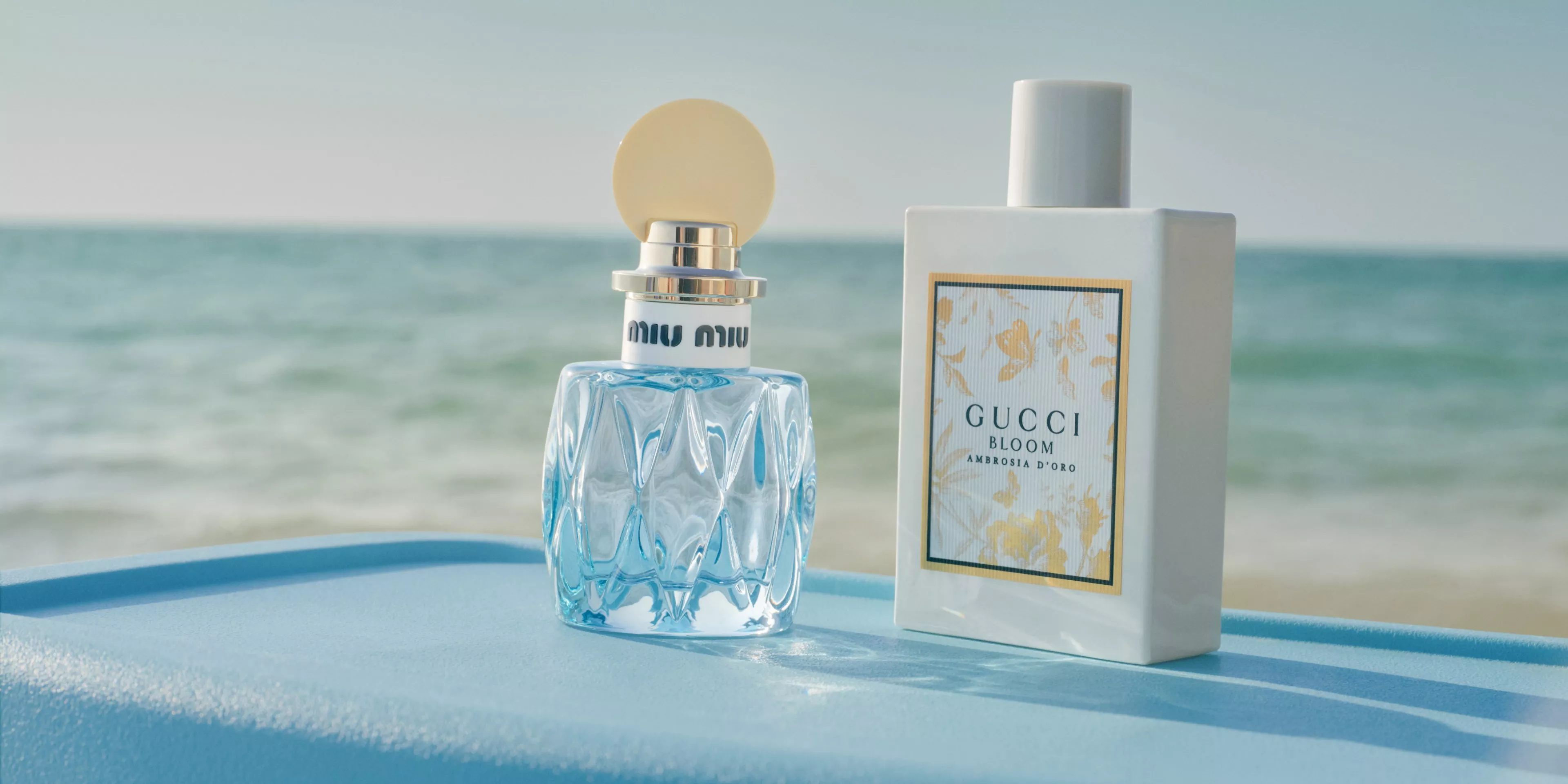 Gucci Bloom Ambrosia d’Oro perfume bottle and box on a blue surface with the sea in the background