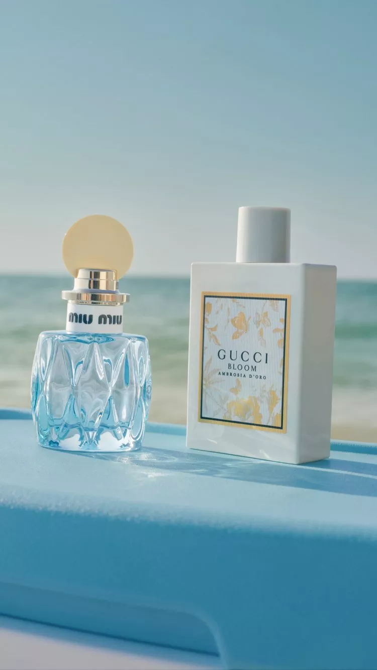 Miu Miu perfume bottle and Gucci Bloom Ambrosia d’Oro fragrance on a blue ledge by the sea backdrop