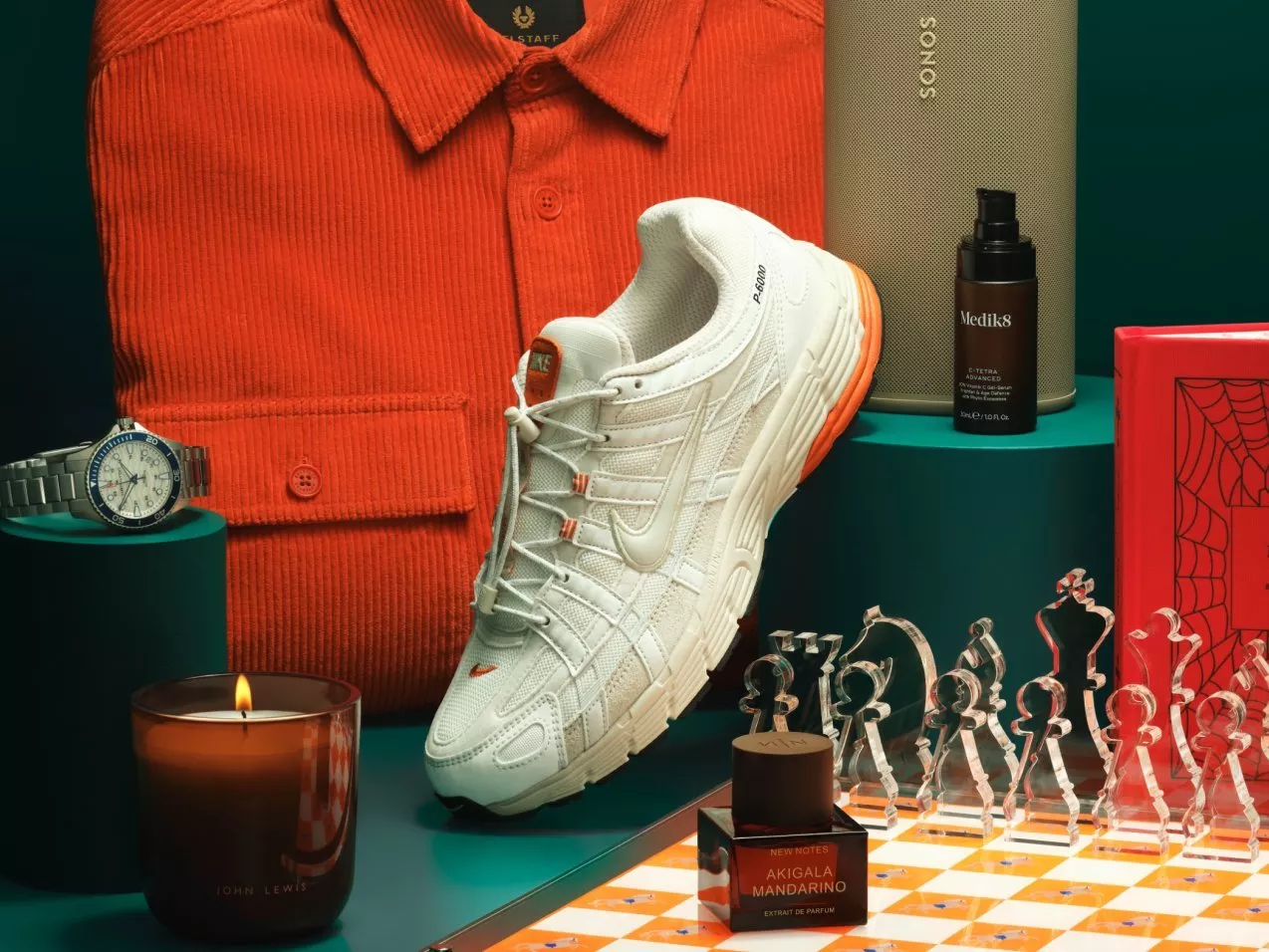 White Nike trainer with orange accents beside Sonos speaker, watch, candle, skincare and chess set gift display
