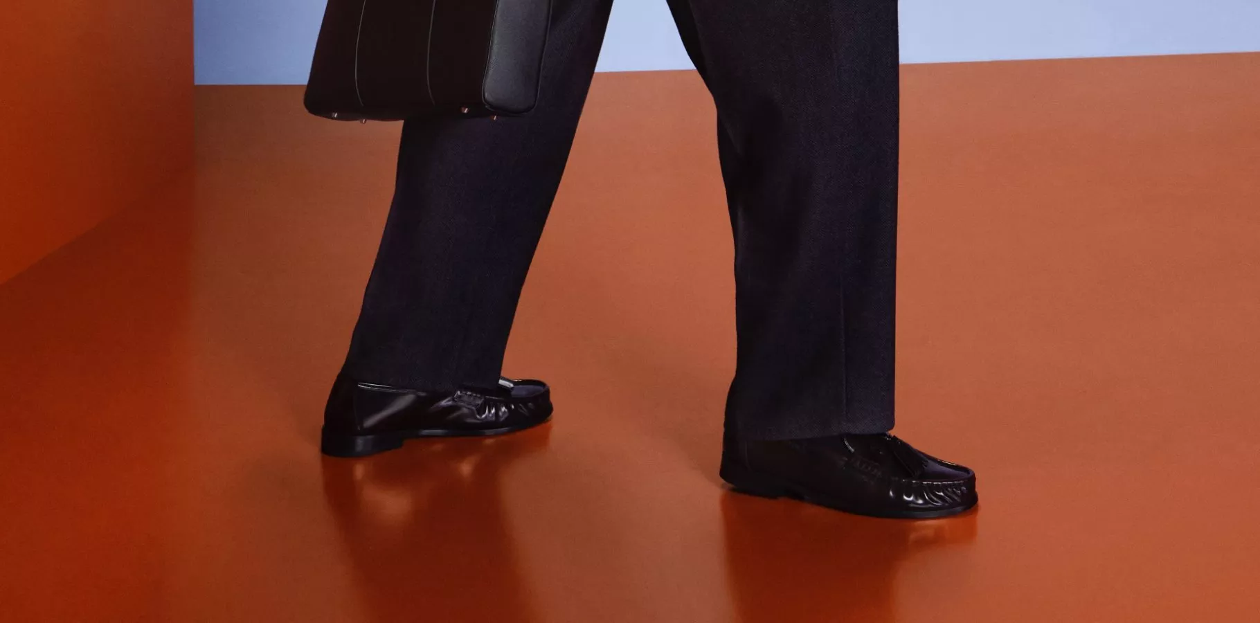 Close-up of black leather loafers with tailored trousers on an orange floor, modern menswear fashion shot