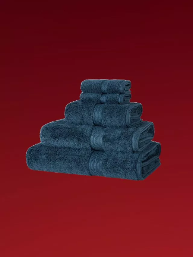 Stacked navy blue cotton towel set with bath towels, hand towels and face cloths on deep red background