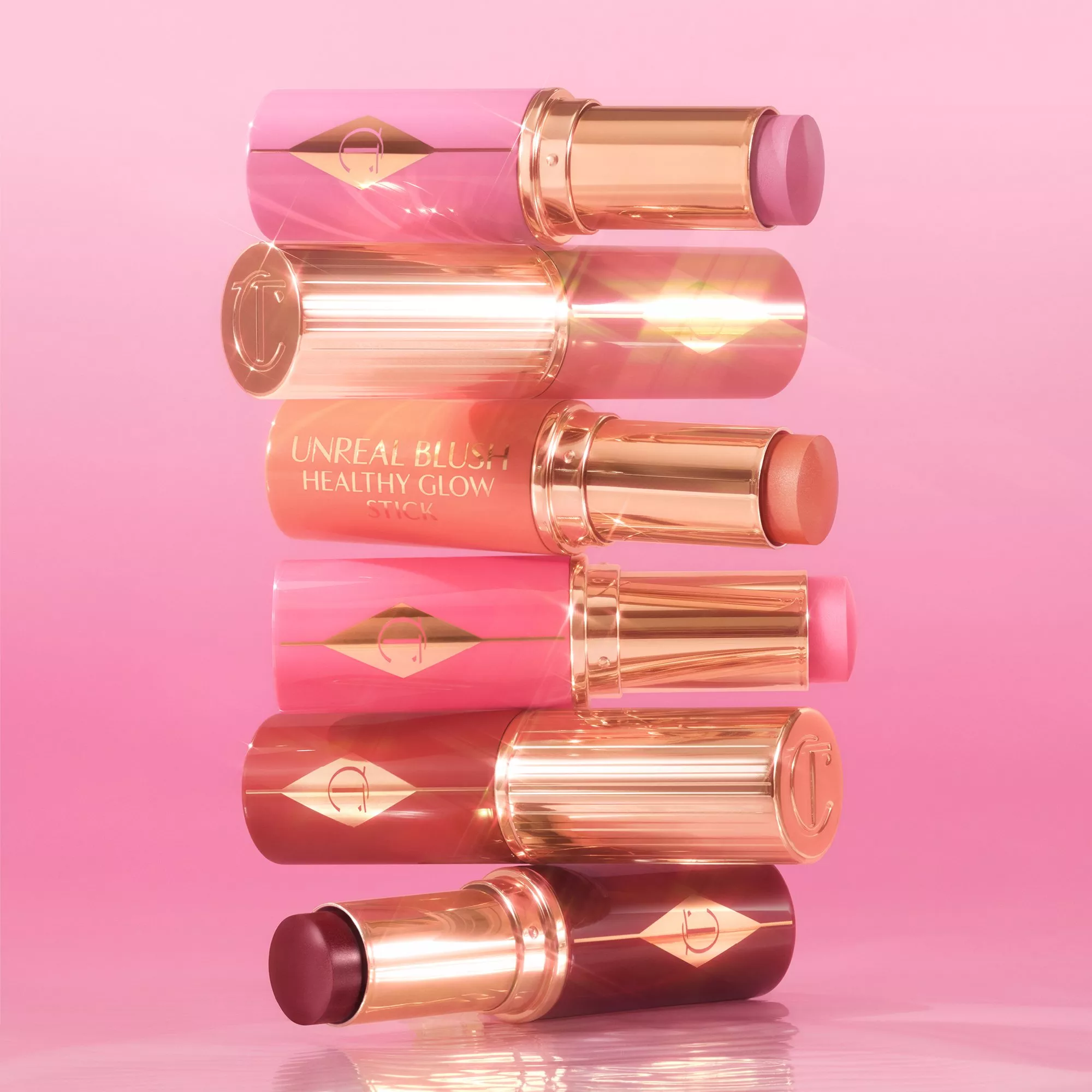 A stack of colourful blush sticks with gold accents on a pink background, showcasing different shades.