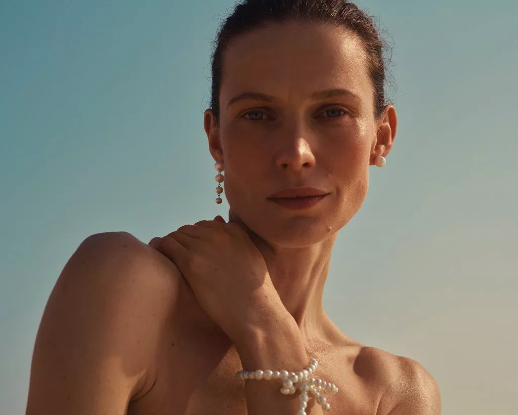 Close-up portrait of woman wearing pearl earrings and bracelet, sunlit minimalist beauty jewellery photo outdoors