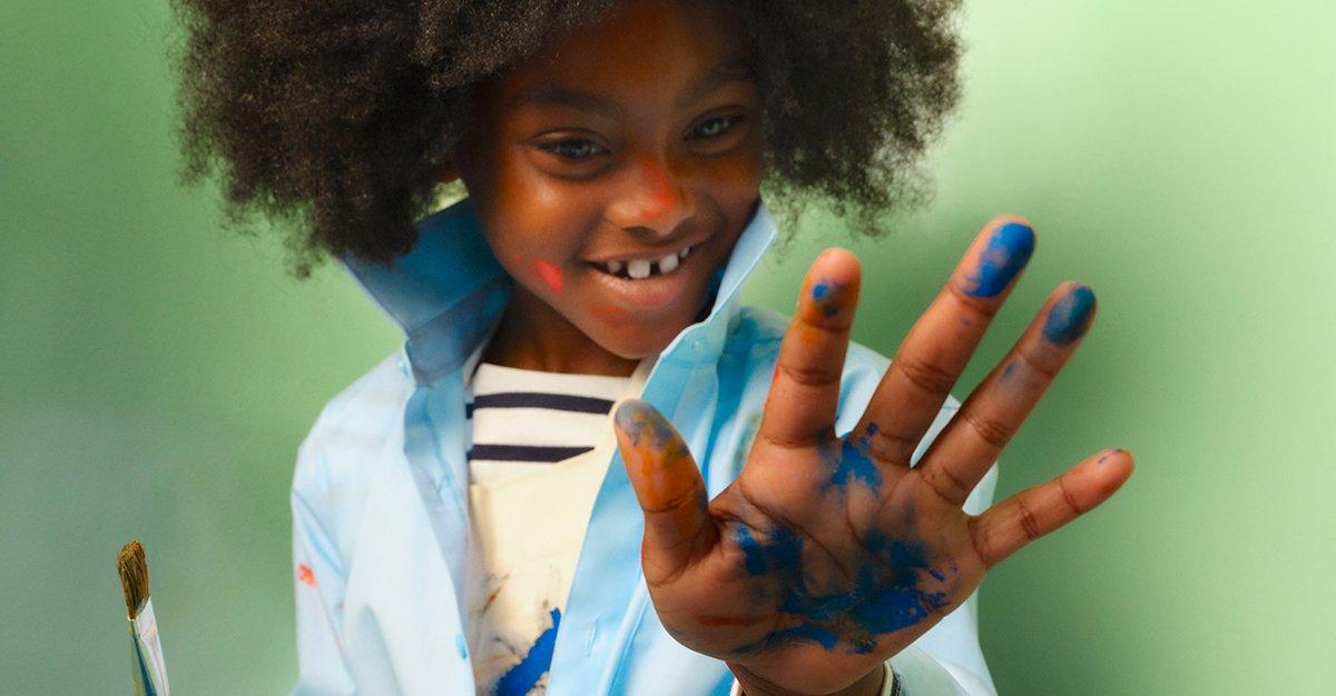 Smiling child showing a paint-covered hand and brush.
