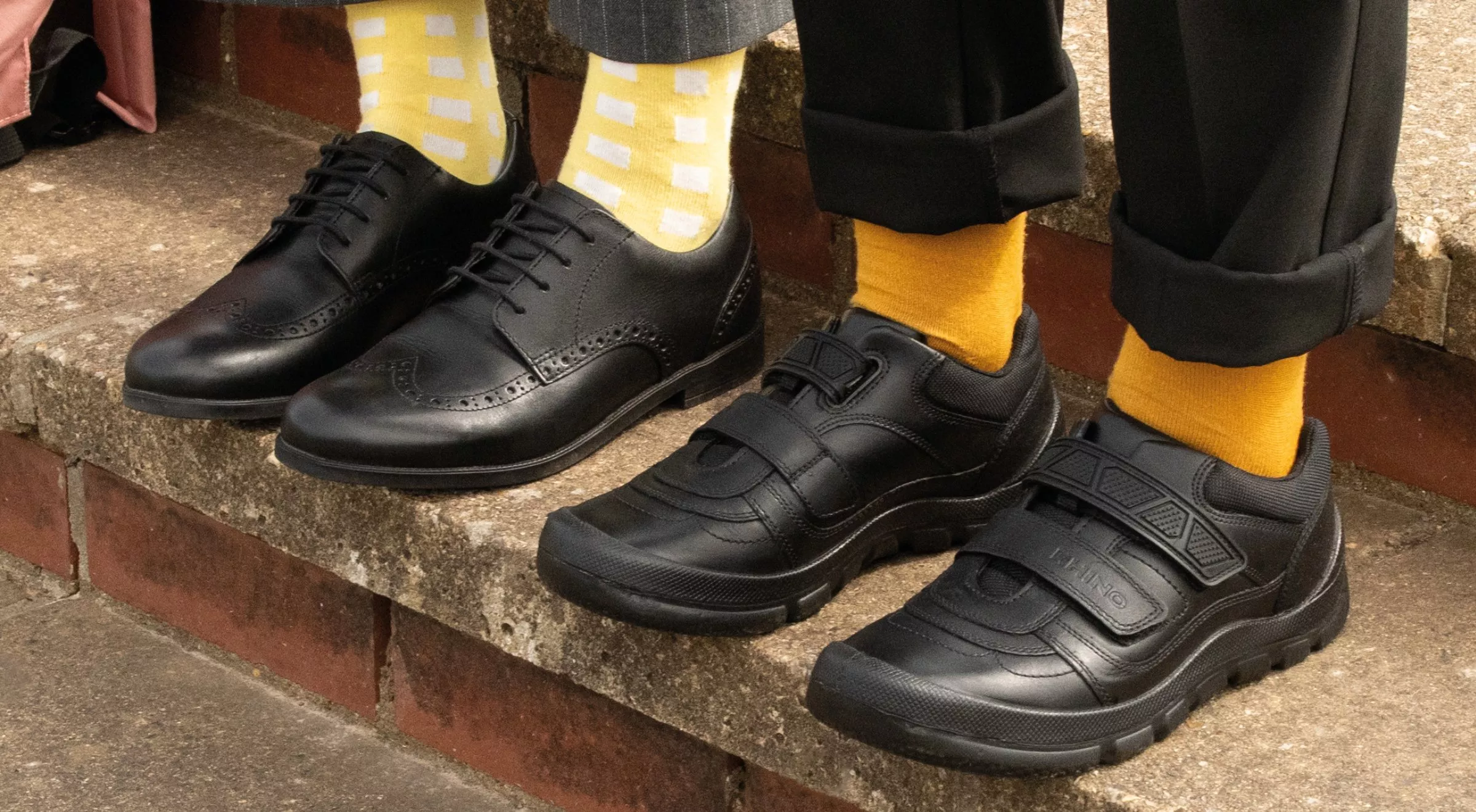 Children wearing black school shoes with bright yellow socks, sitting on brick steps outside school building