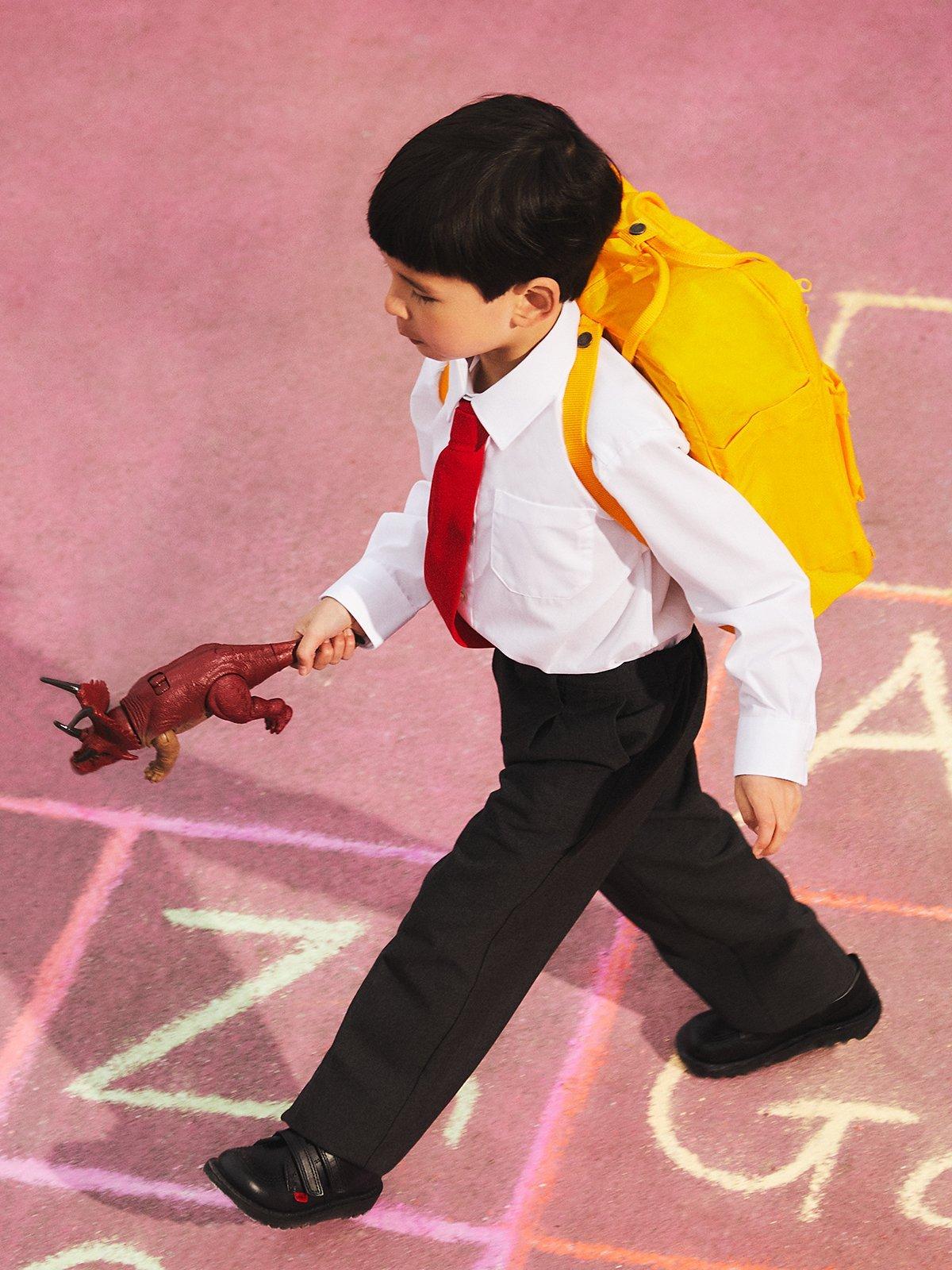 Boy walking across the playground with a yellow backcpack