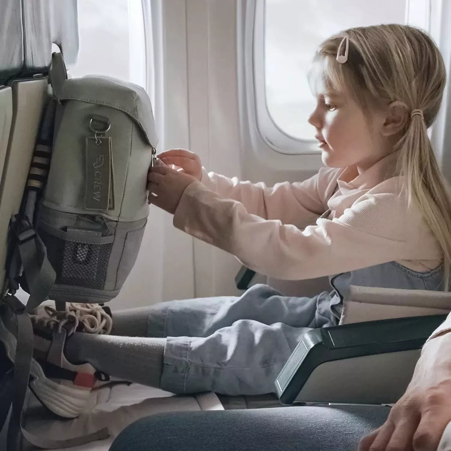 girl sitting in an airplane seat playing with the backpack in front of her