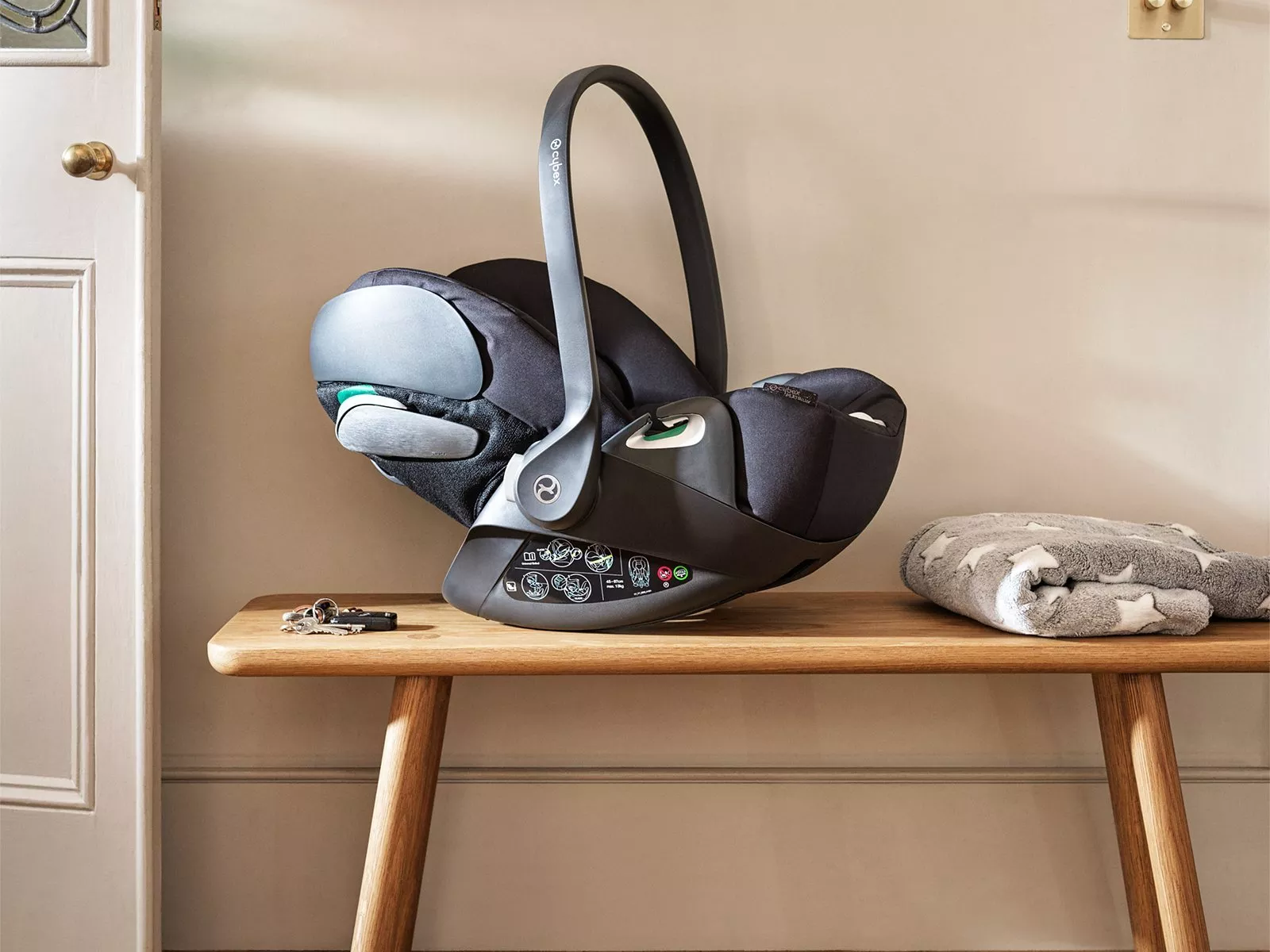 A black car seat with a handle rests on a wooden bench next to folded grey star-patterned blanket.
