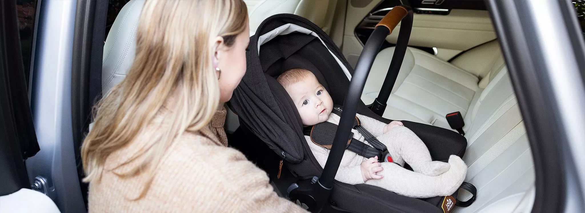 Mother securing baby in an infant car seat in a modern car, showing safe travel and child car seat safety