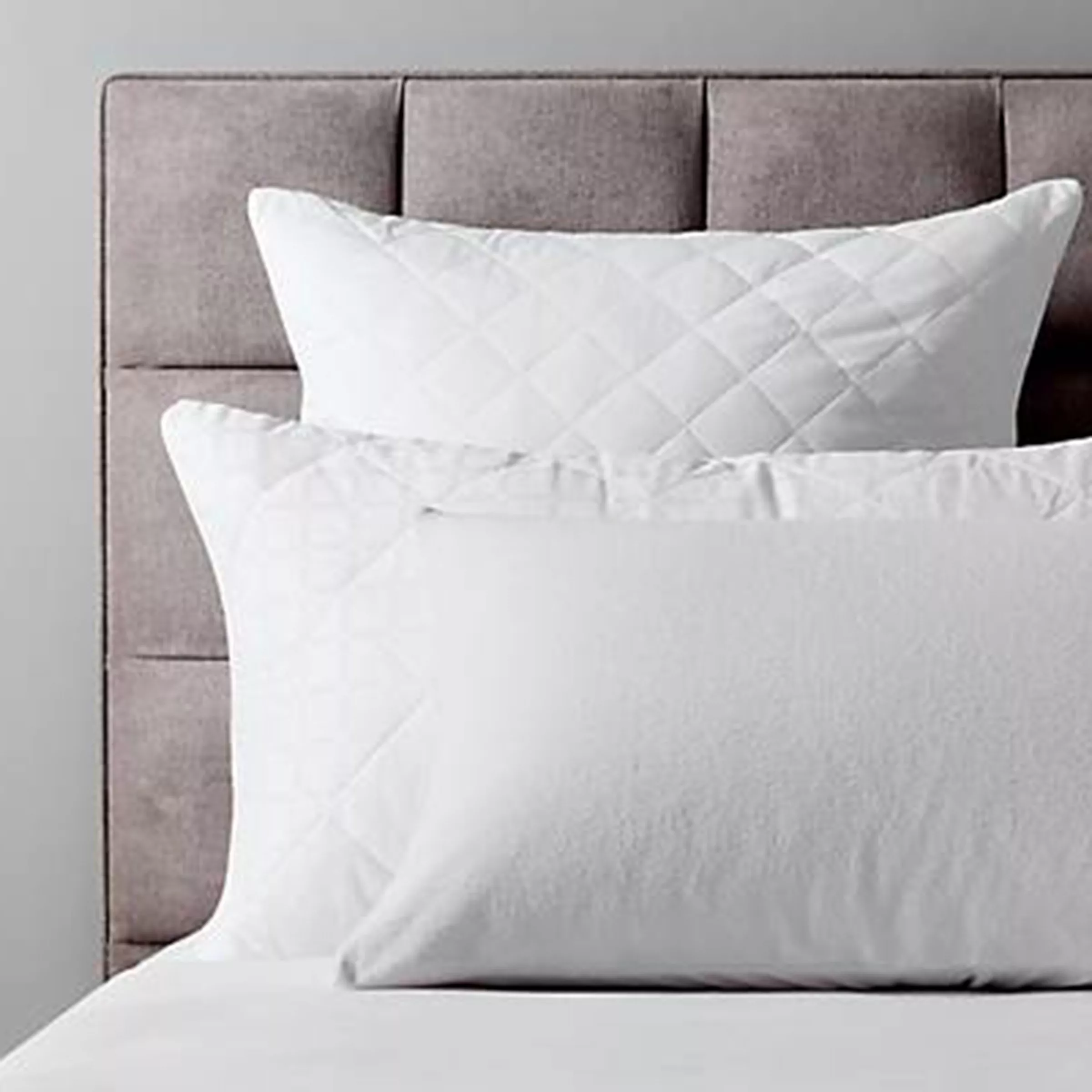 Modern grey upholstered headboard with white quilted pillows, creating a stylish and cosy bedroom look.