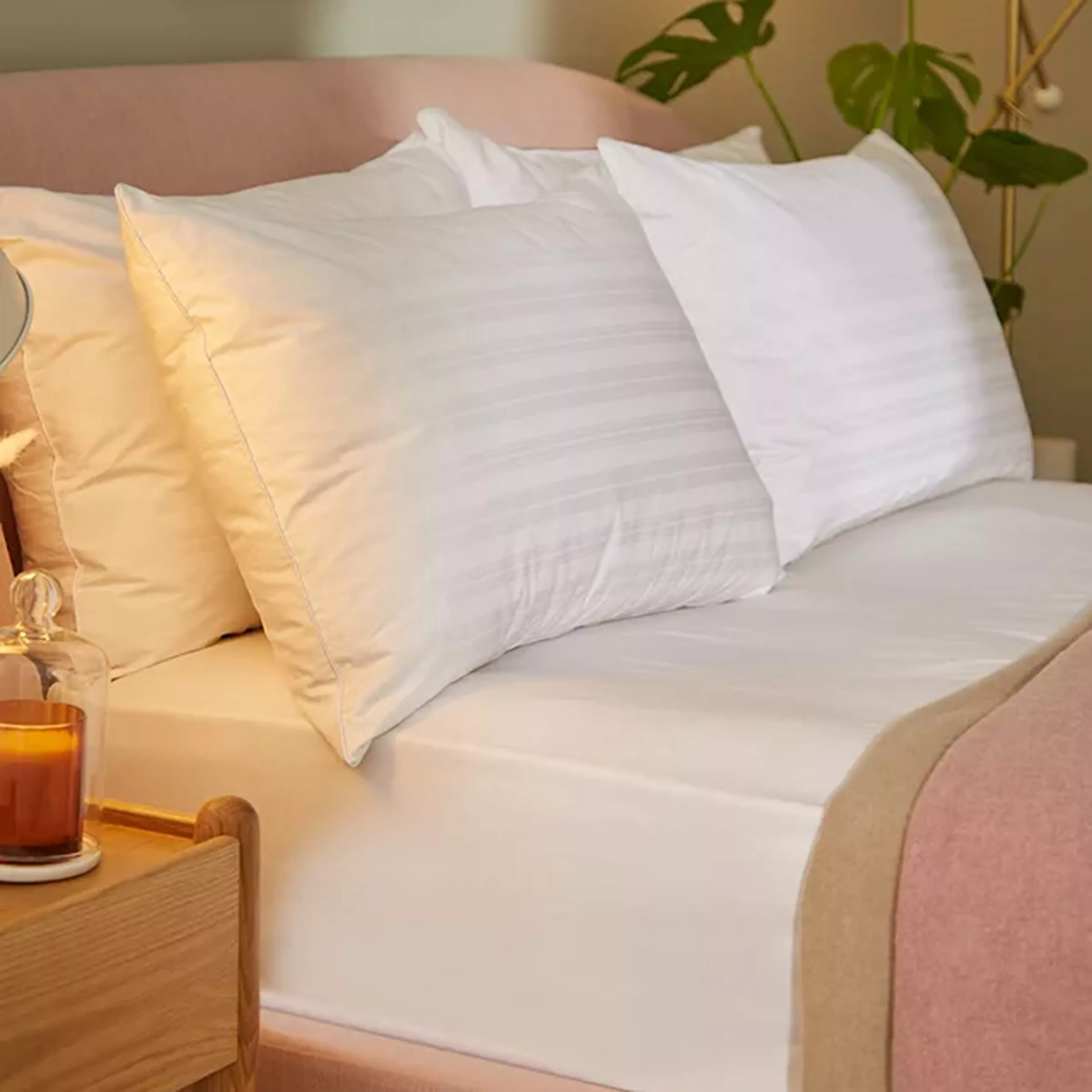 Cosy bedroom setting with white pillows on a neatly made bed. A wooden nightstand holds a candle.