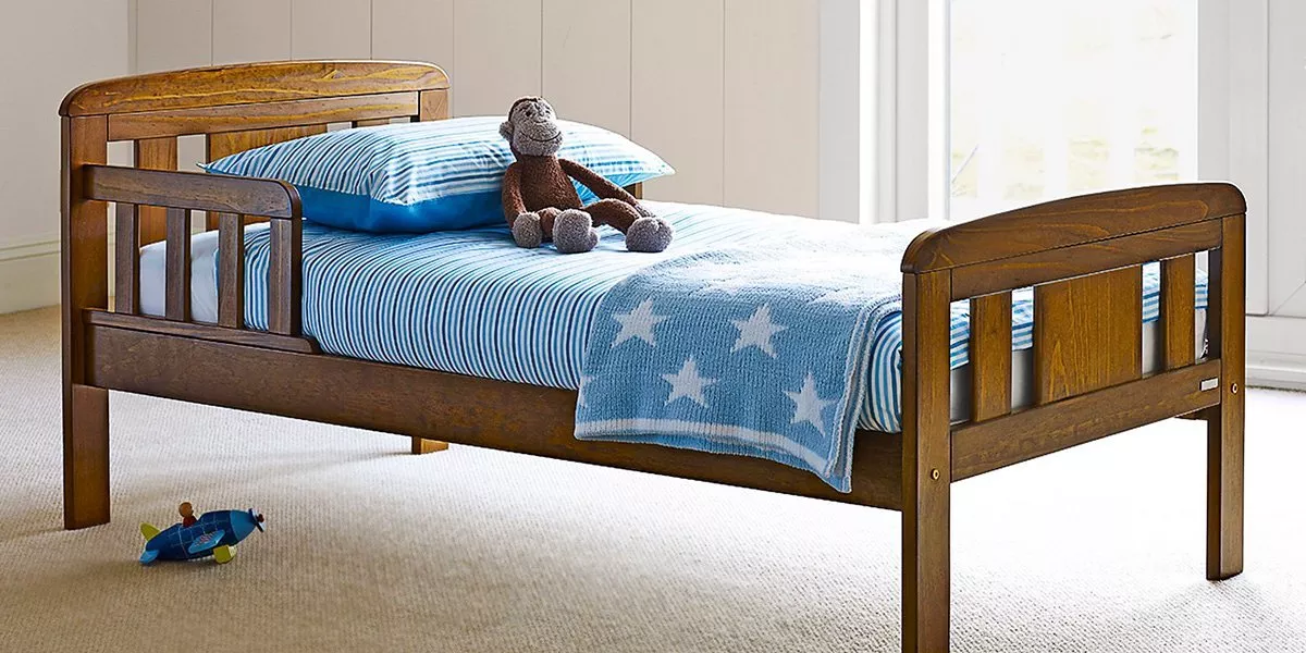 Wooden toddler bed with side rails, blue striped bedding and star blanket in a bright children's bedroom
