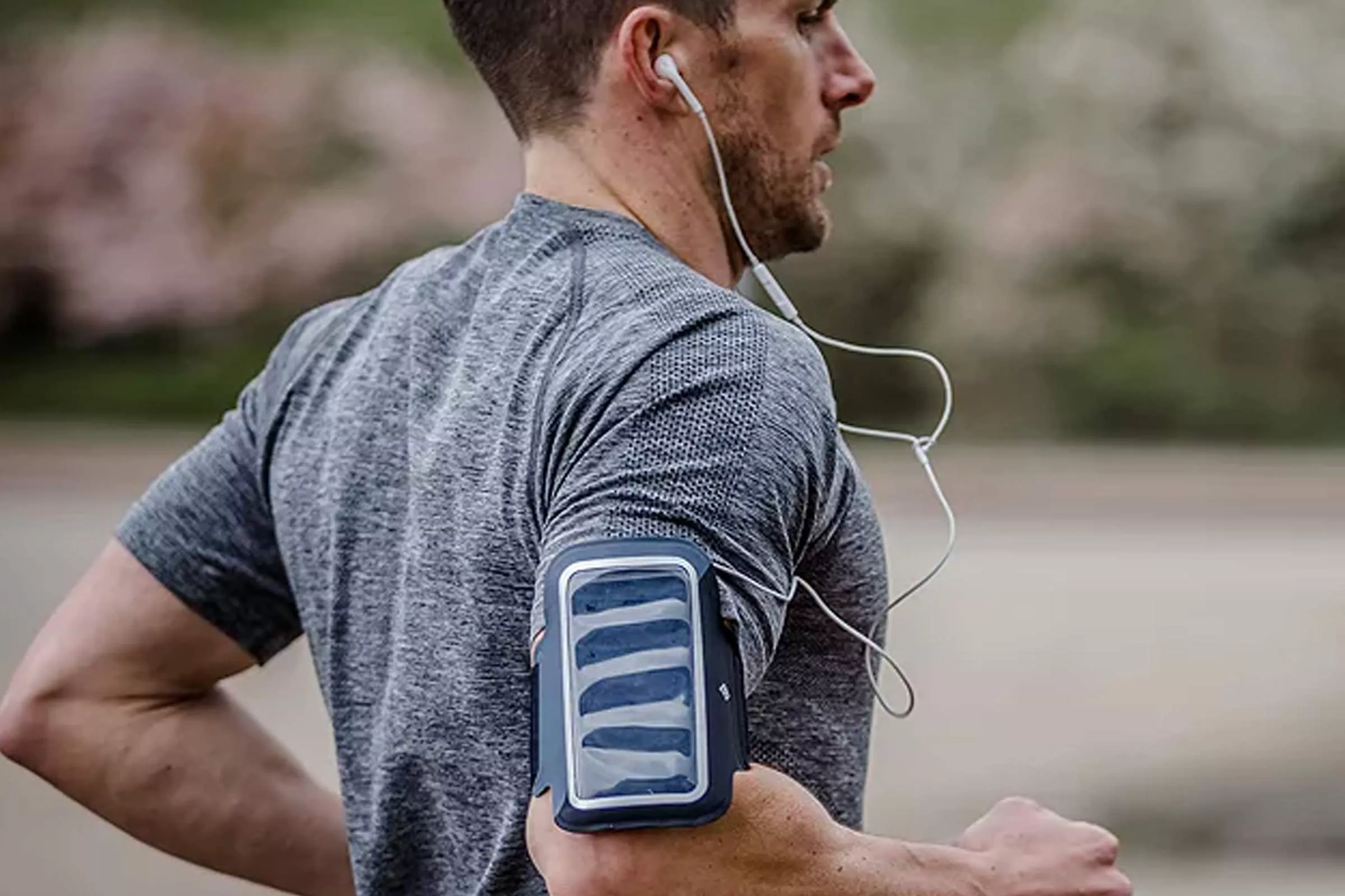 Man running outdoors wearing wired earphones and an armband phone holder, fitness training on a trail path