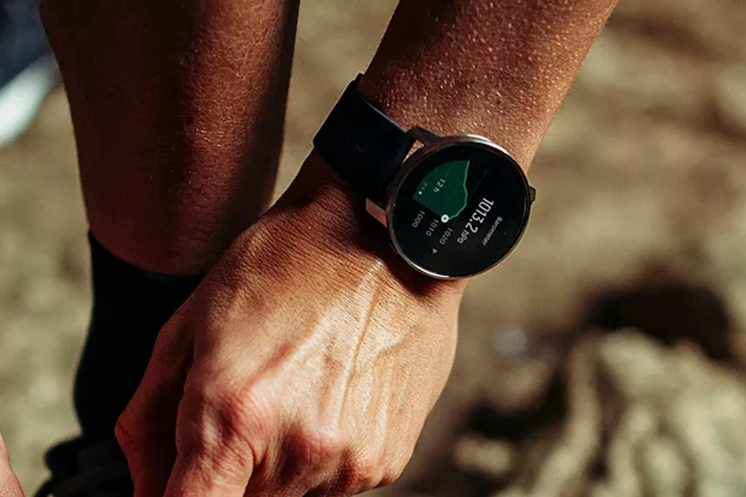 Close-up of a runner’s wrist wearing a GPS sports smartwatch showing training stats outdoors on a sunny day
