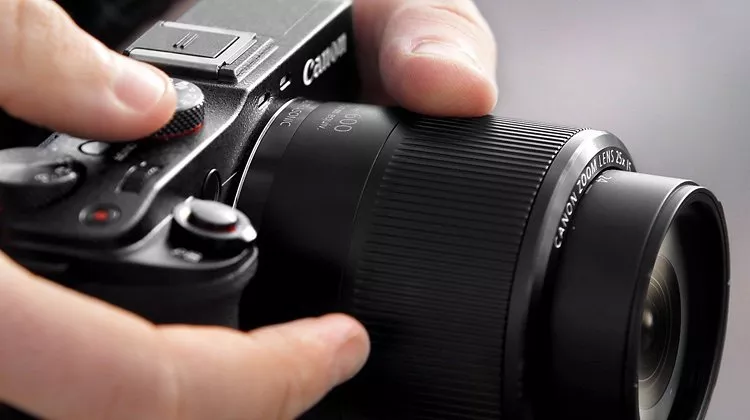 Close-up of hands adjusting a Canon camera lens, showcasing controls and textured grip for precise photography.