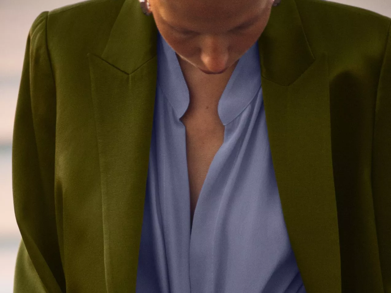 A close-up of a person wearing an olive green blazer over a light blue blouse, showing a V-neck style.