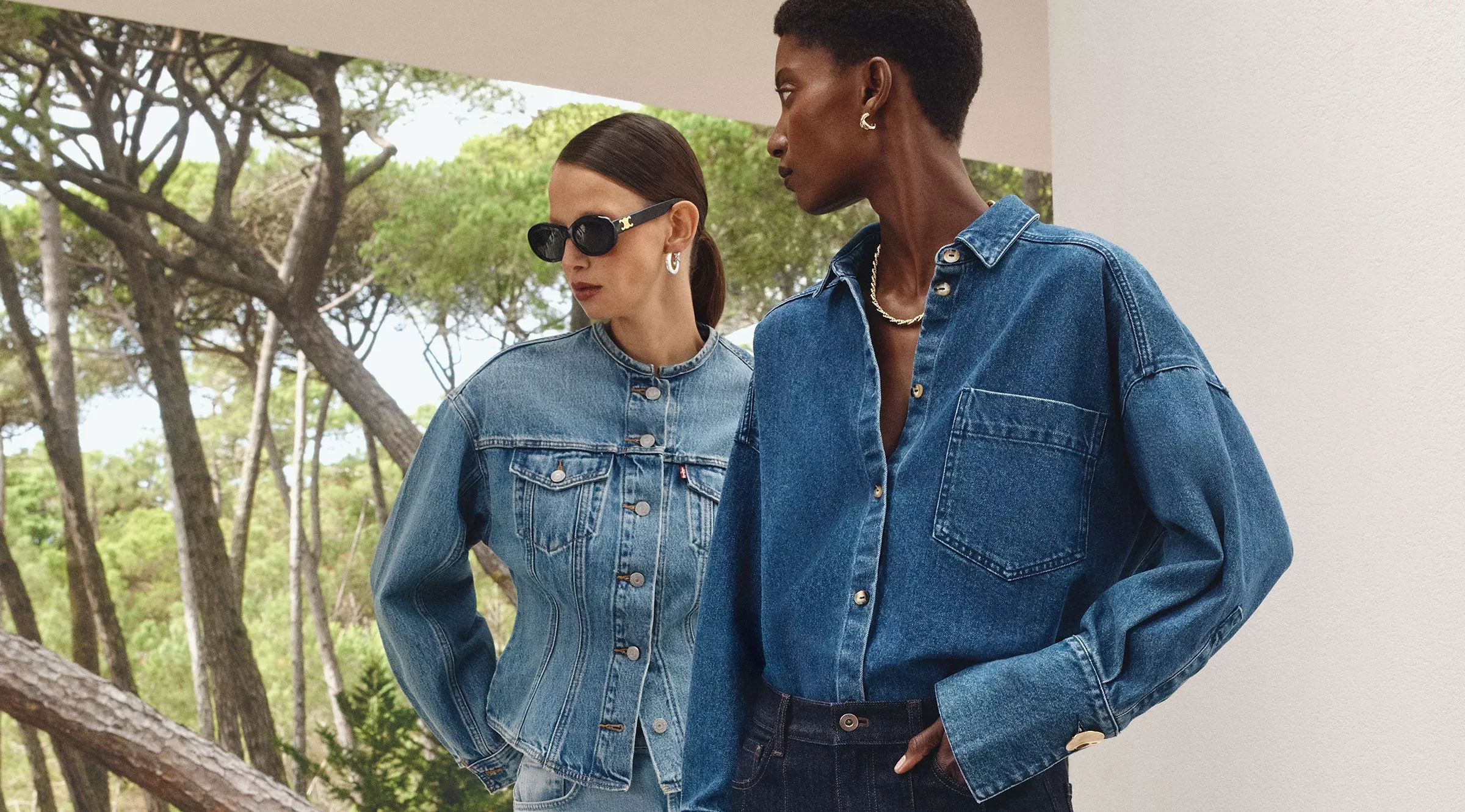 Fashionable denim outfits with button-up shirts outdoors. Trees frame the stylish scene elegantly.