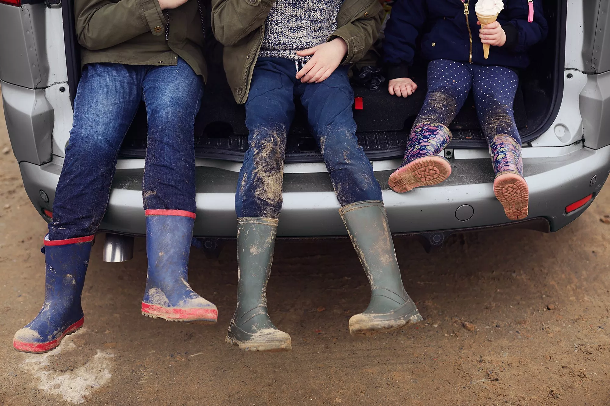 Three pairs of muddy boots hang from a car boot, showcasing a messy outdoor adventure.