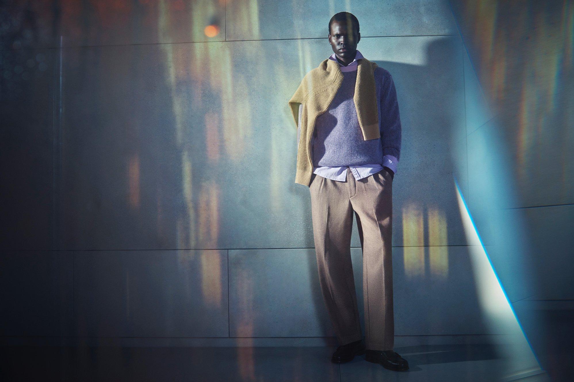 Male model wearing smart trousers, a shirt and cashmere jumper with another cashmere jumper draped over his shoulders