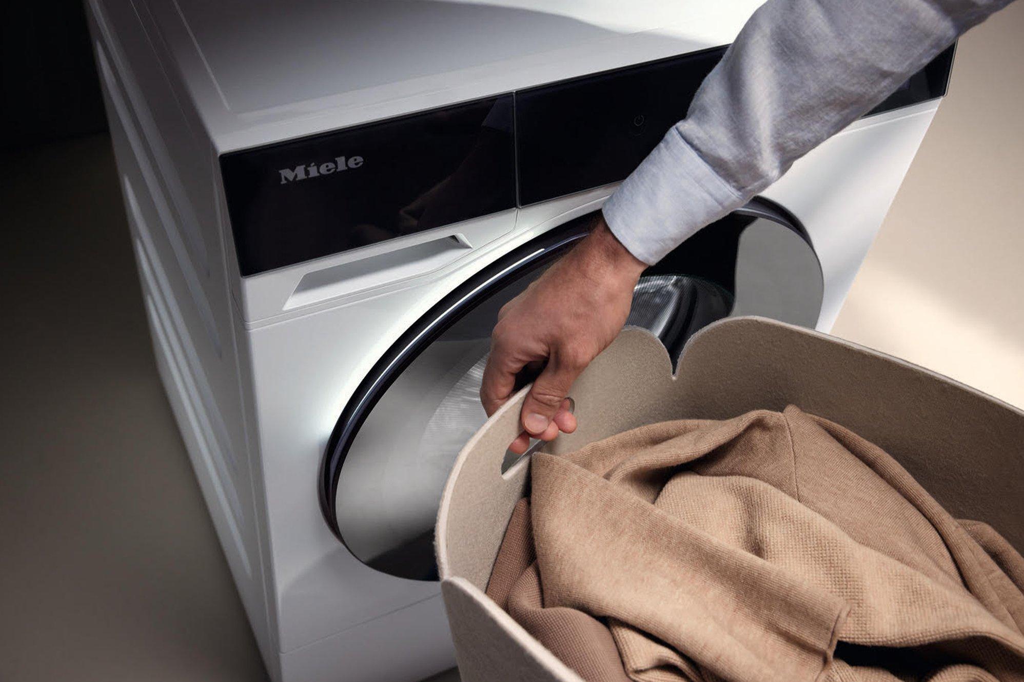 A neutrally decorated laundry room with two washing machines and a jute rug and plant in the foreground