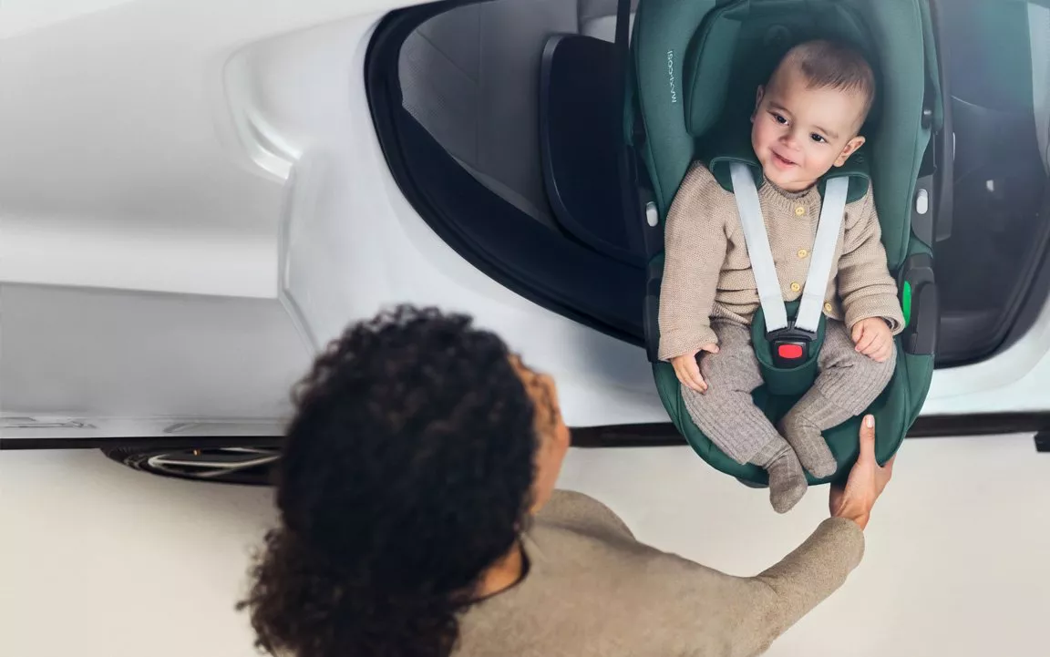 Parent lifting smiling baby in rear-facing infant car seat beside open car door, demonstrating child car safety.